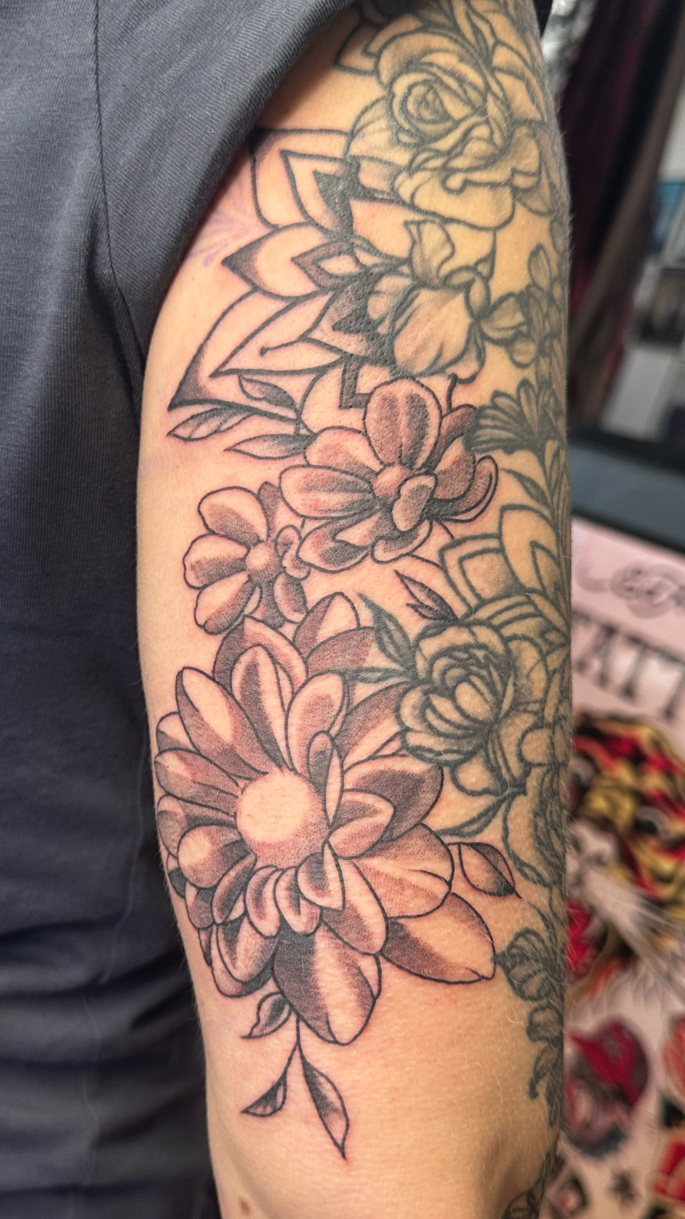 Black and gray floral tattoo sleeve featuring roses, peonies, and leaves on a person's upper arm.