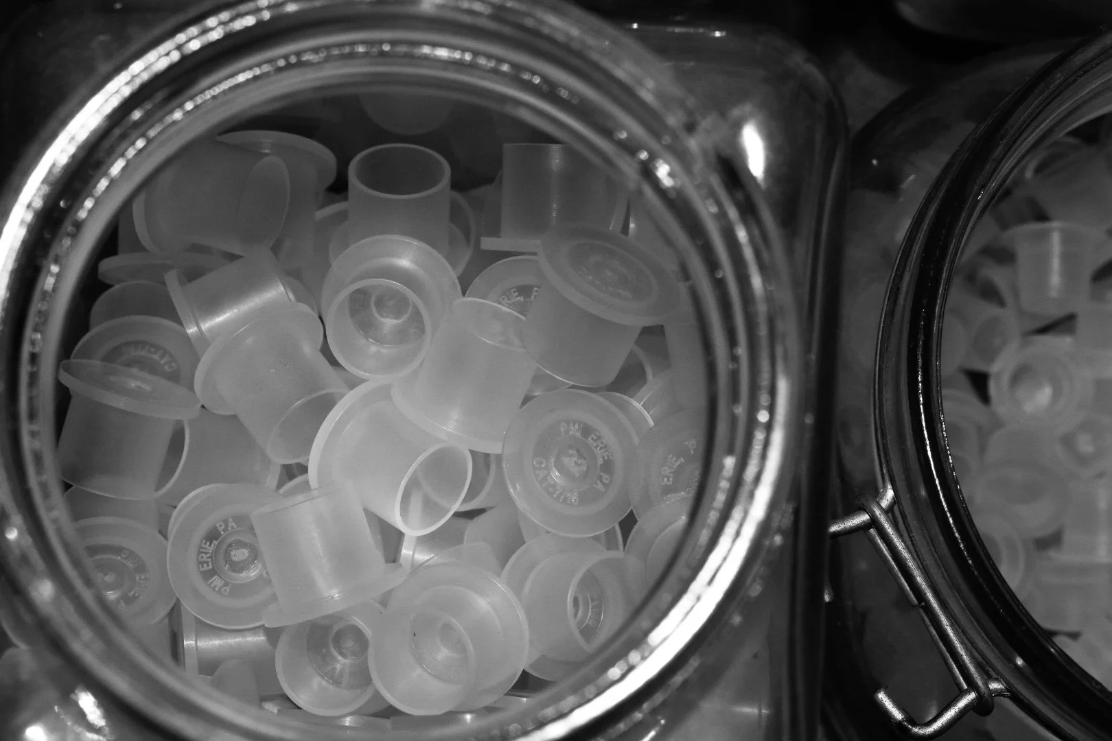 Close-up view of a glass jar filled with small plastic caps or lid pieces, with other jars partially visible in the background.