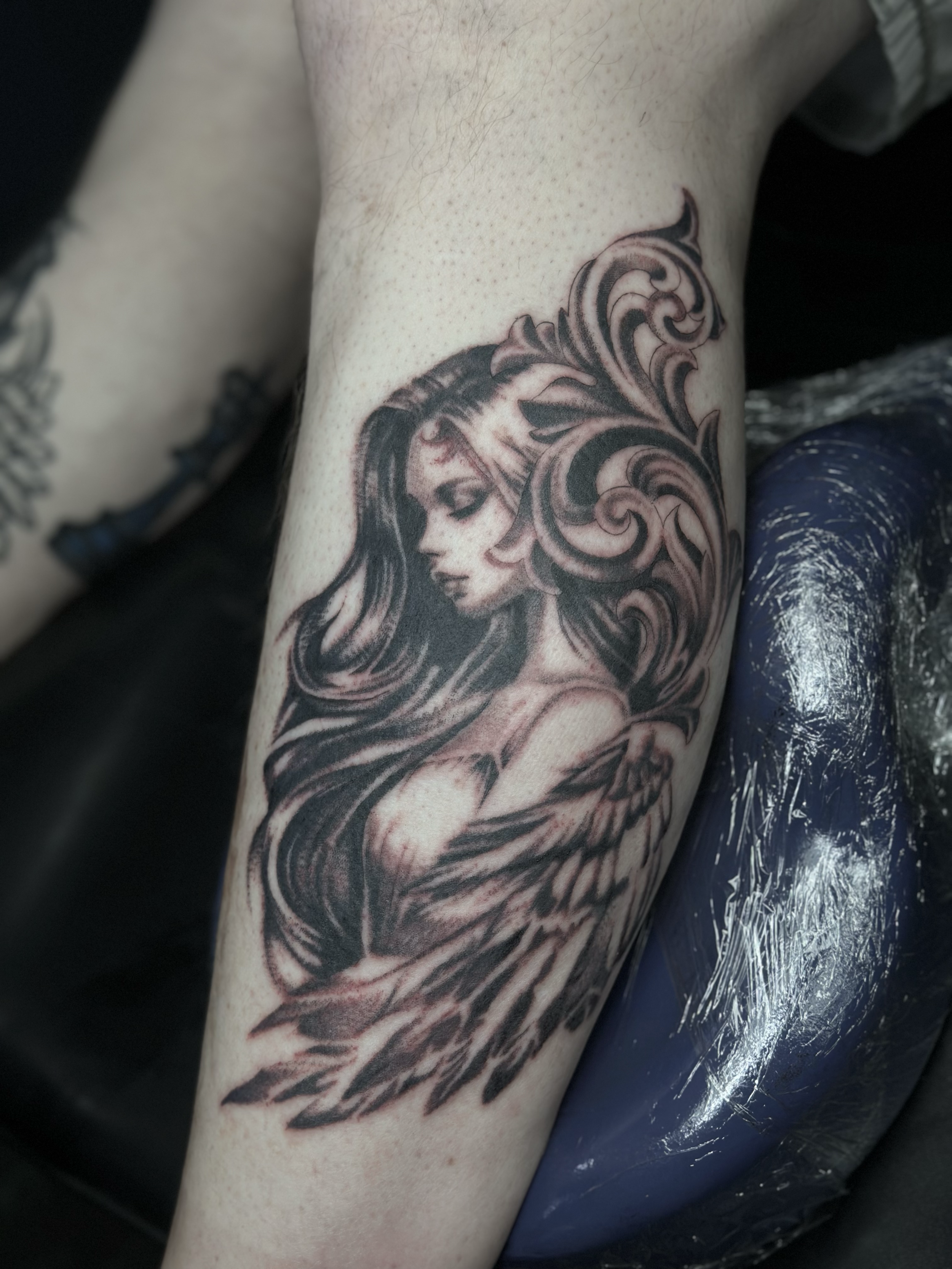 Tattoo of a woman with long flowing hair and angel wings on her arm.