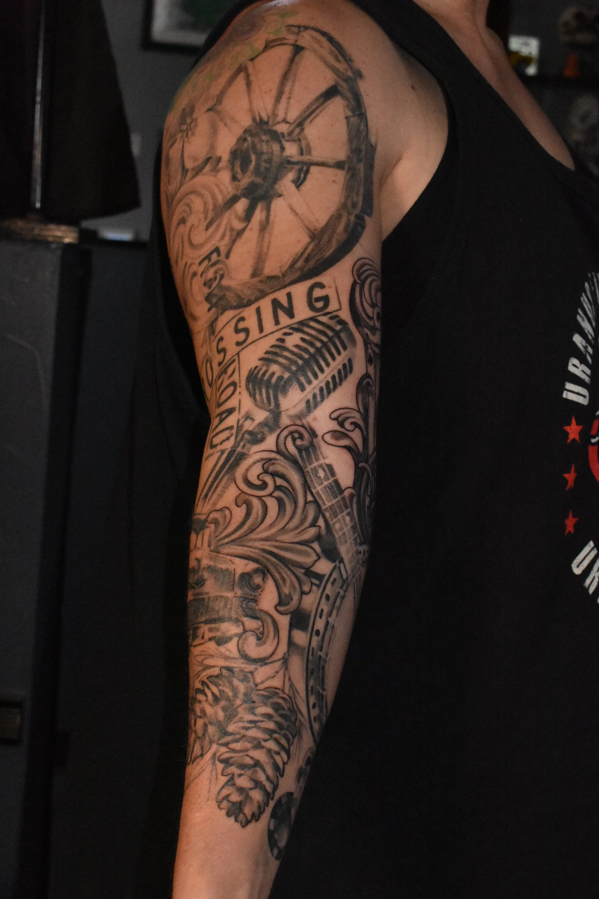 Tattooed arm with a clock, microphone, guitar, and floral designs.