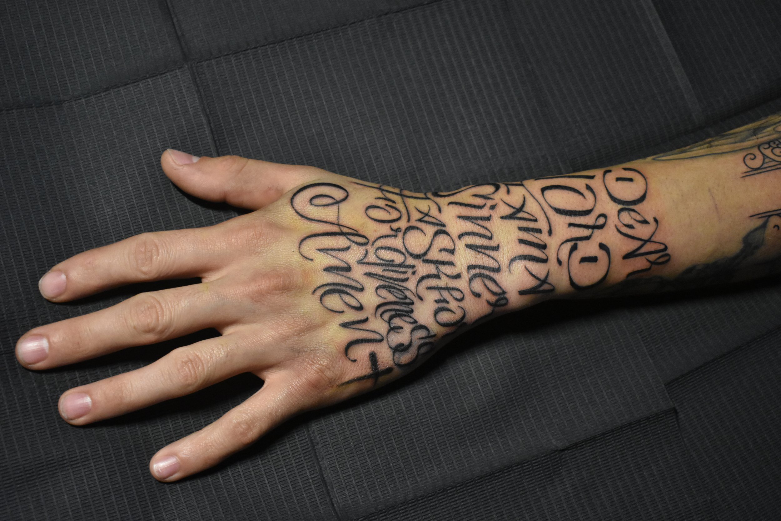 Close-up of a tattooed hand resting on a black textured surface