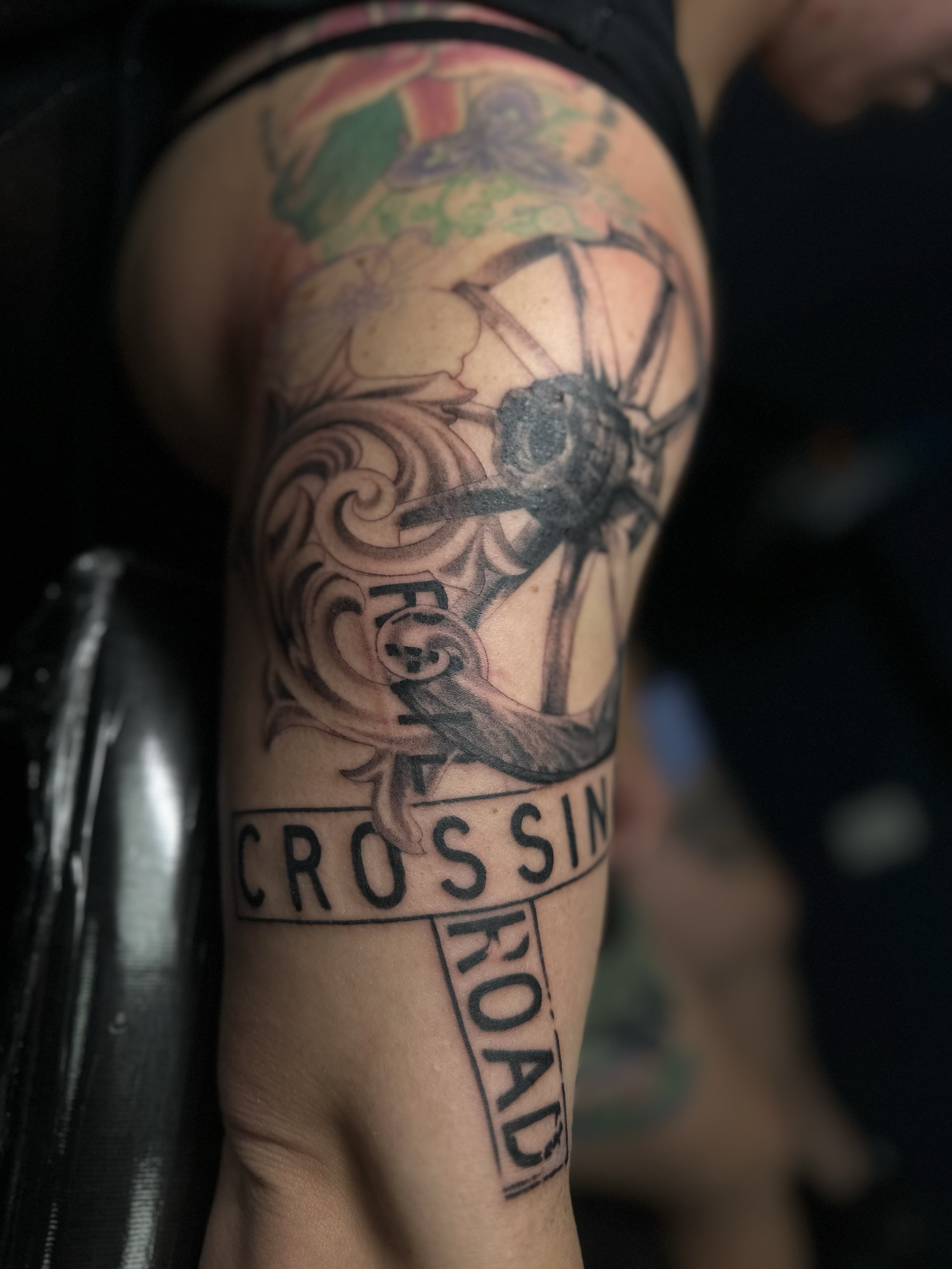 Tattoo of a compass on upper arm with the words 'Cross in Road'.