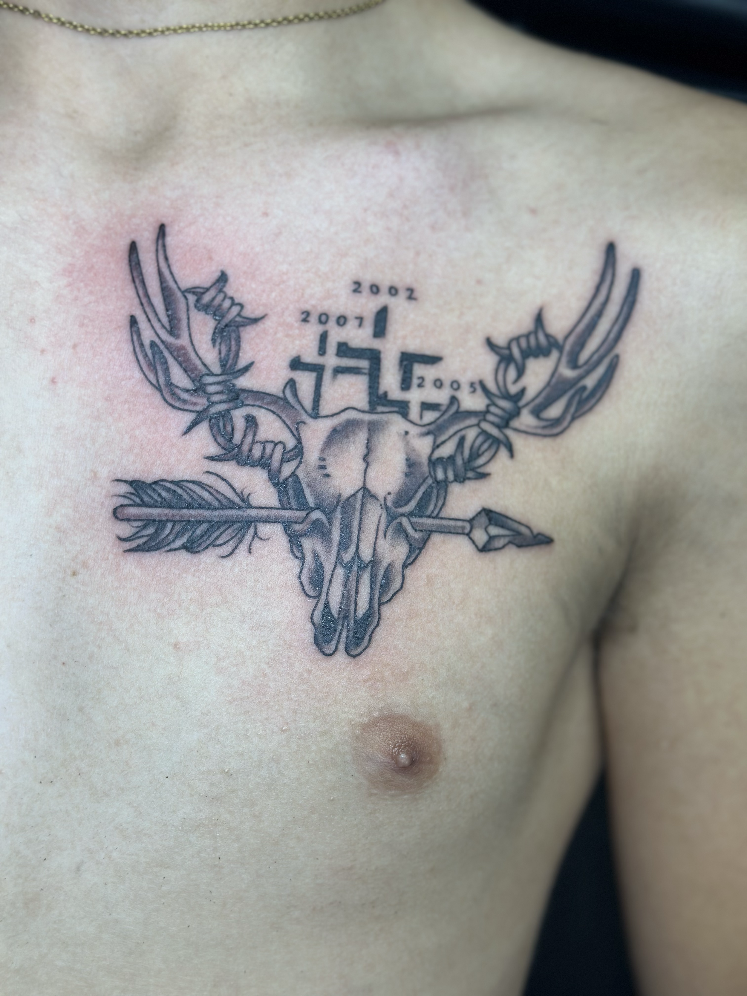 Tattoo of a deer skull with antlers, an arrow pierced through it, and the years 2005, 2007, 2008, and 2002 above the skull.