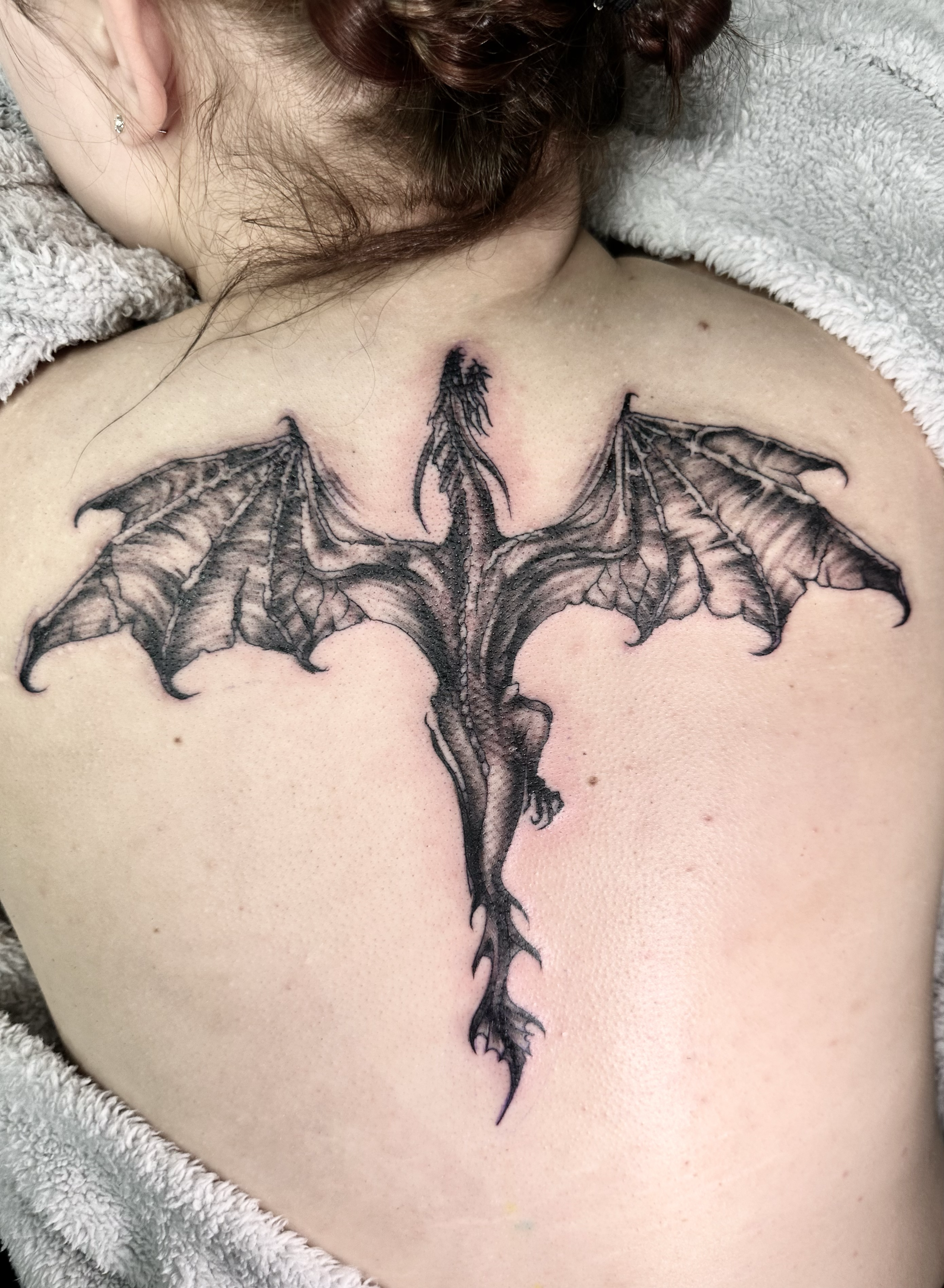 A black and gray tattoo of a dragon with outstretched wings on a person's upper chest.