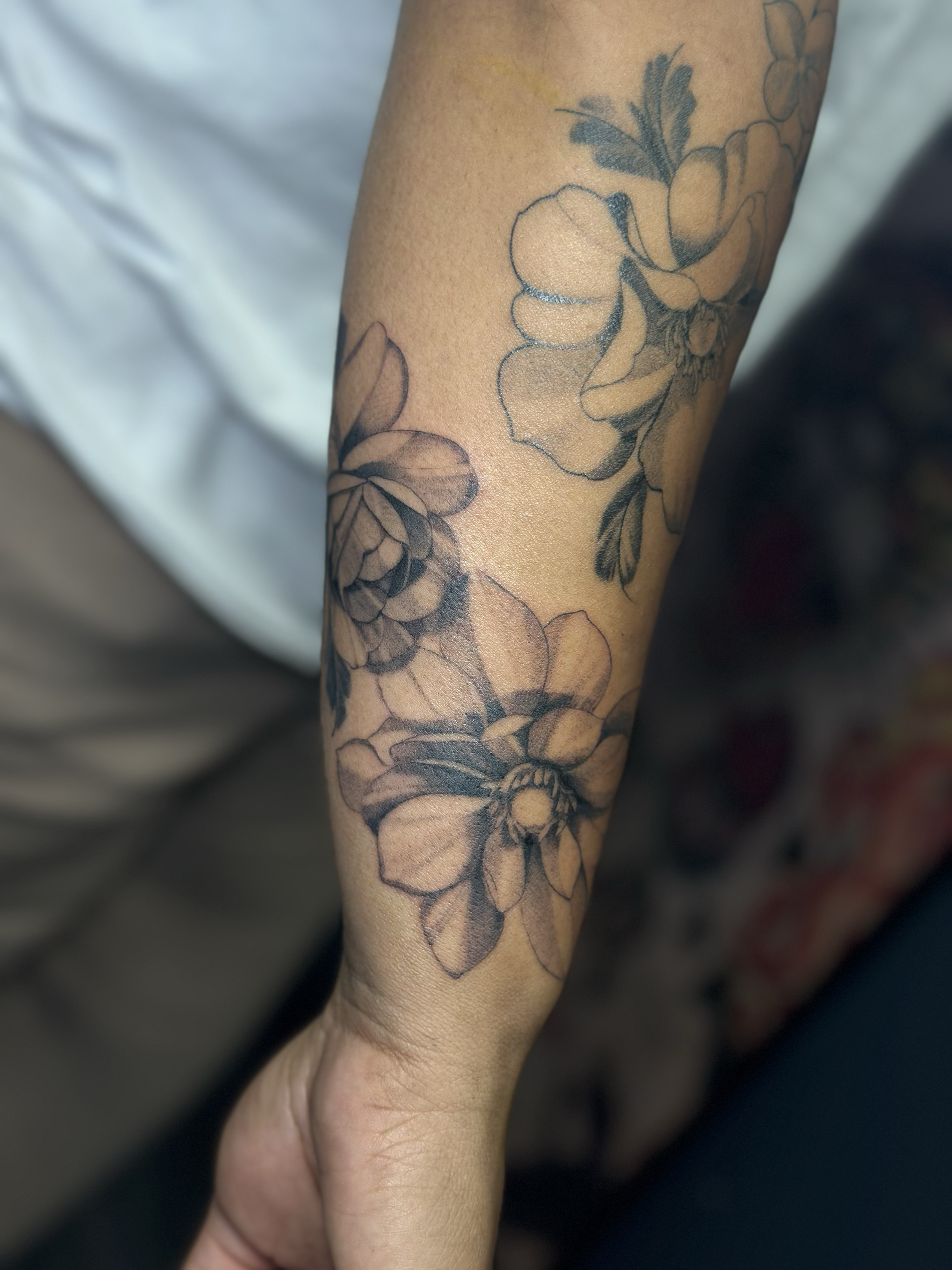 Black and gray floral tattoo on person's forearm, featuring large blooming flowers with detailed petals and leaves.