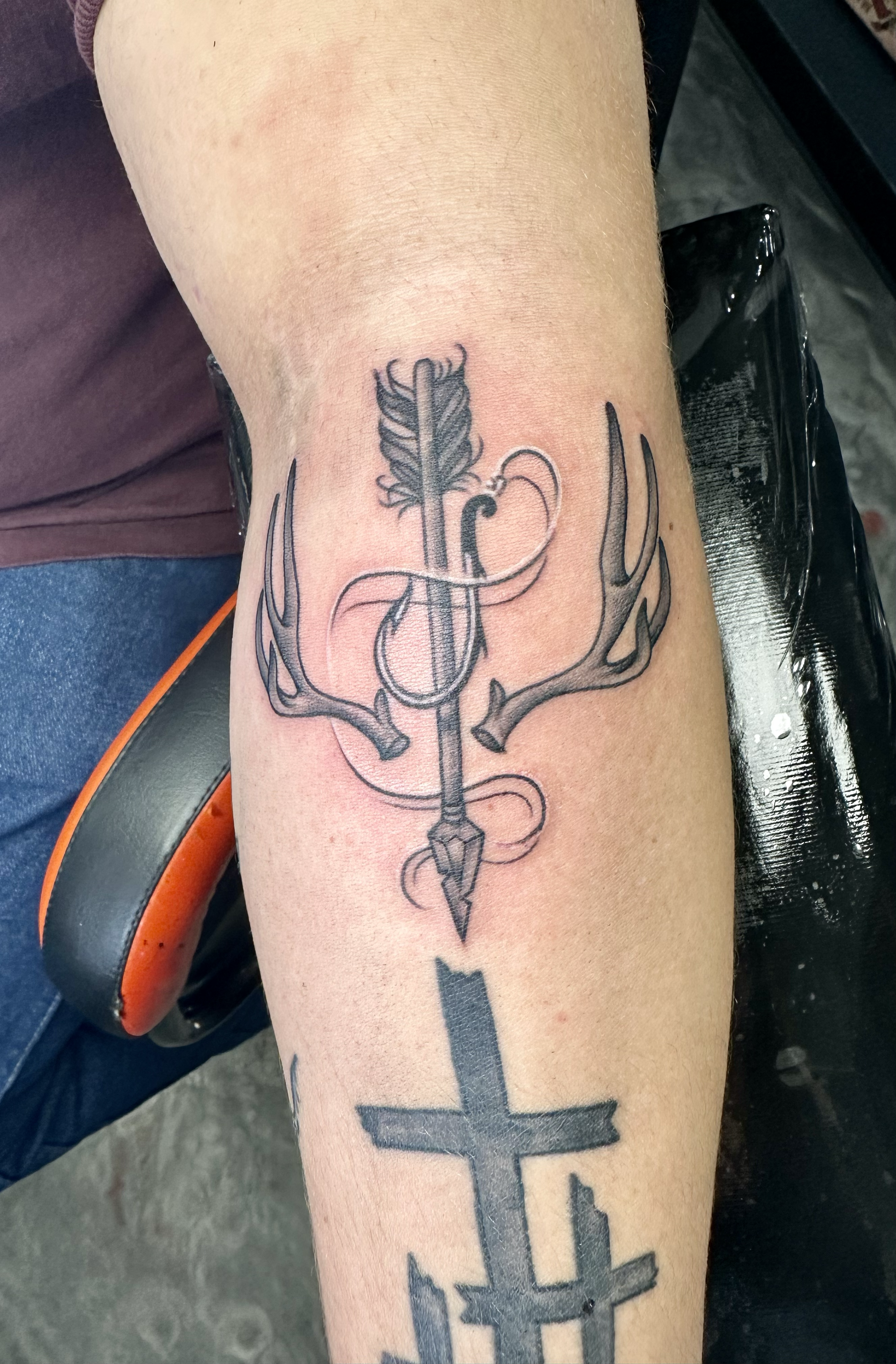 A tattoo on a person's forearm featuring a bow and arrow intertwined with deer antlers.