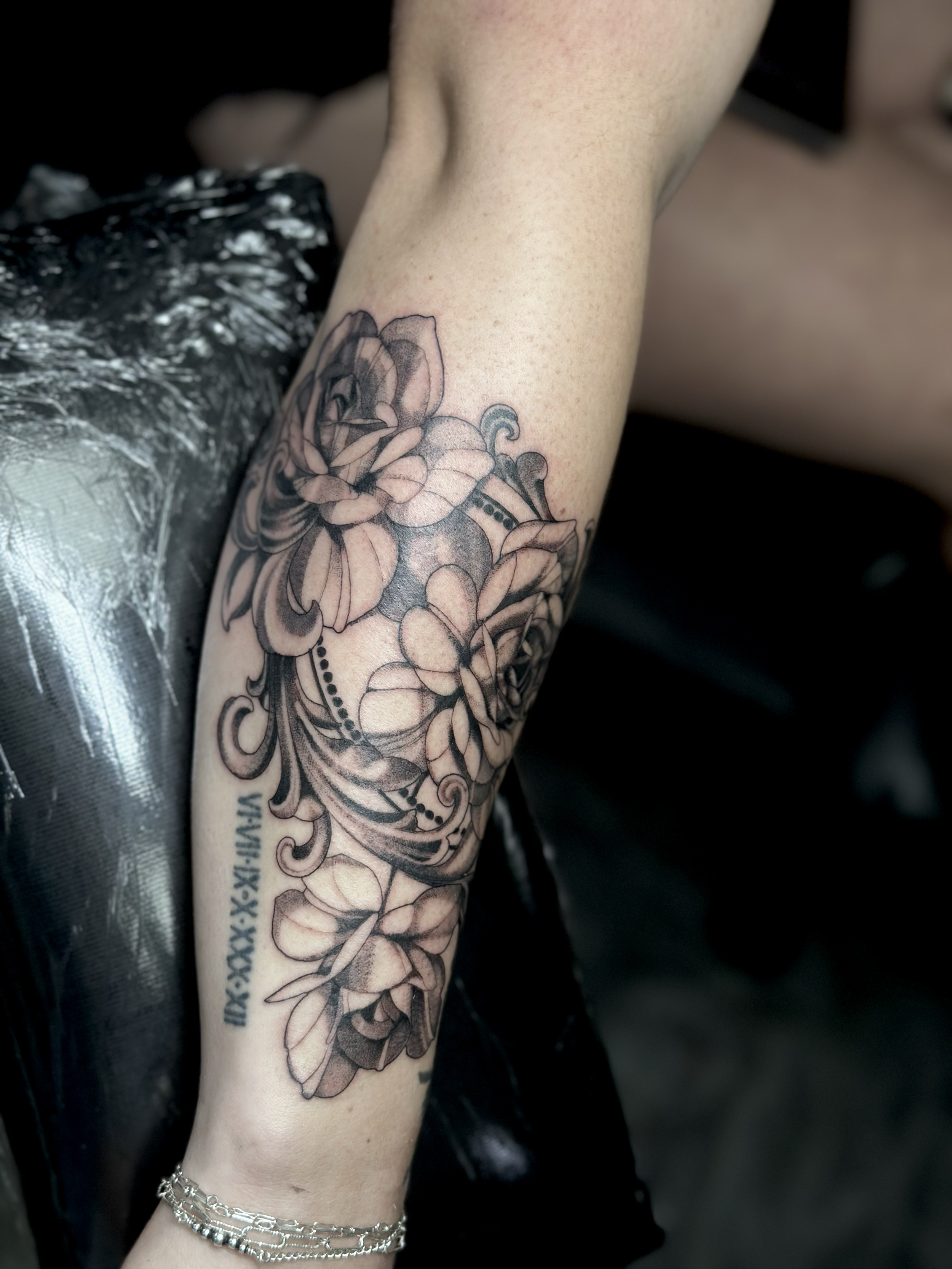 Black and gray floral tattoo on person's forearm with Roman numerals on the lower part.