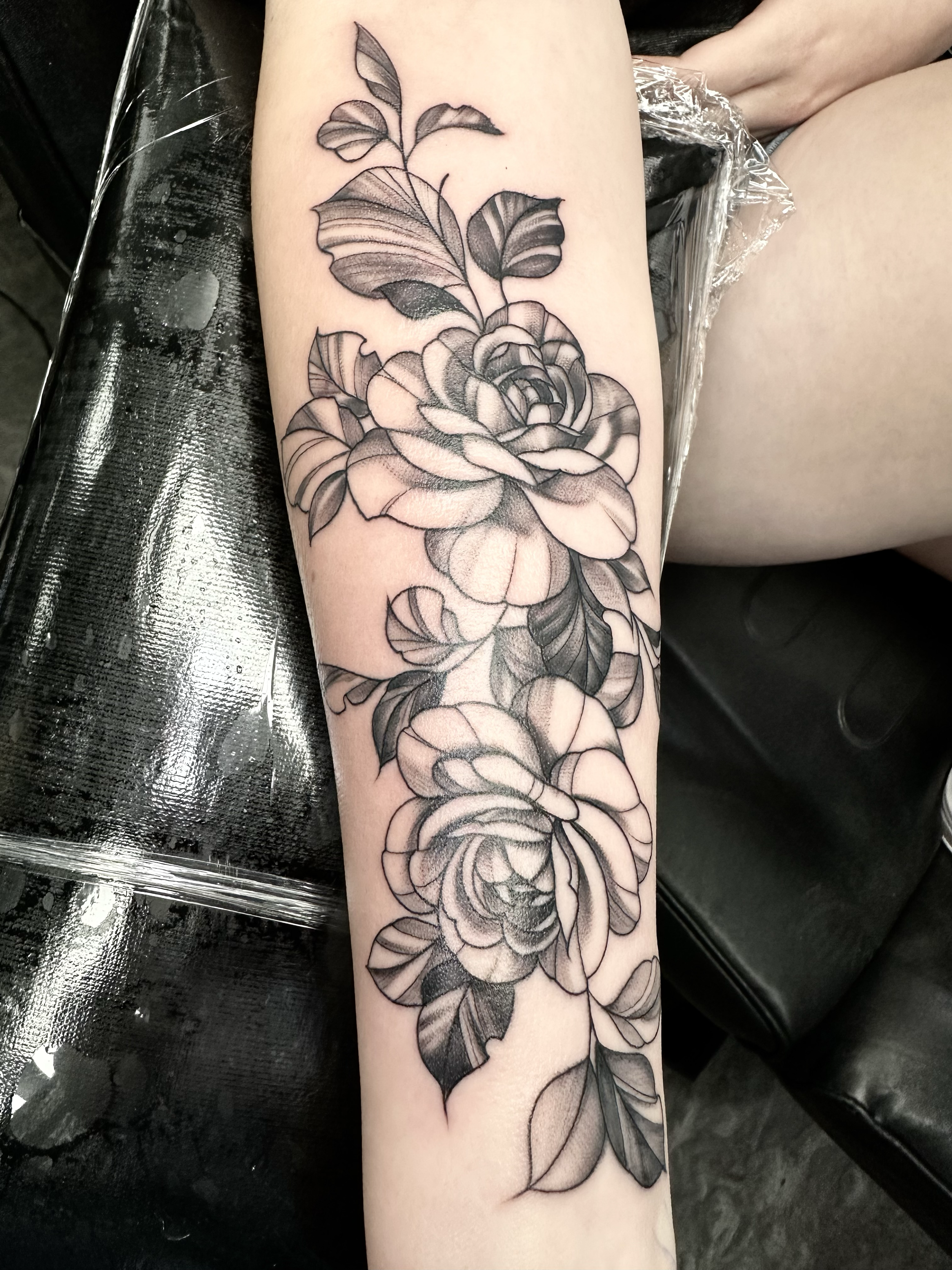 Black and gray floral tattoo of roses and leaves on a person's forearm.