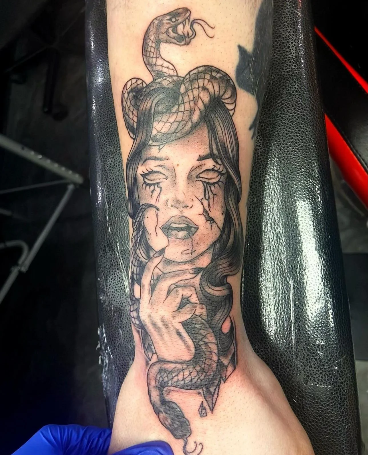 Tattoo of a woman's face with long hair, open eyes with tears, and snakes entwined in her hair and around her hand.