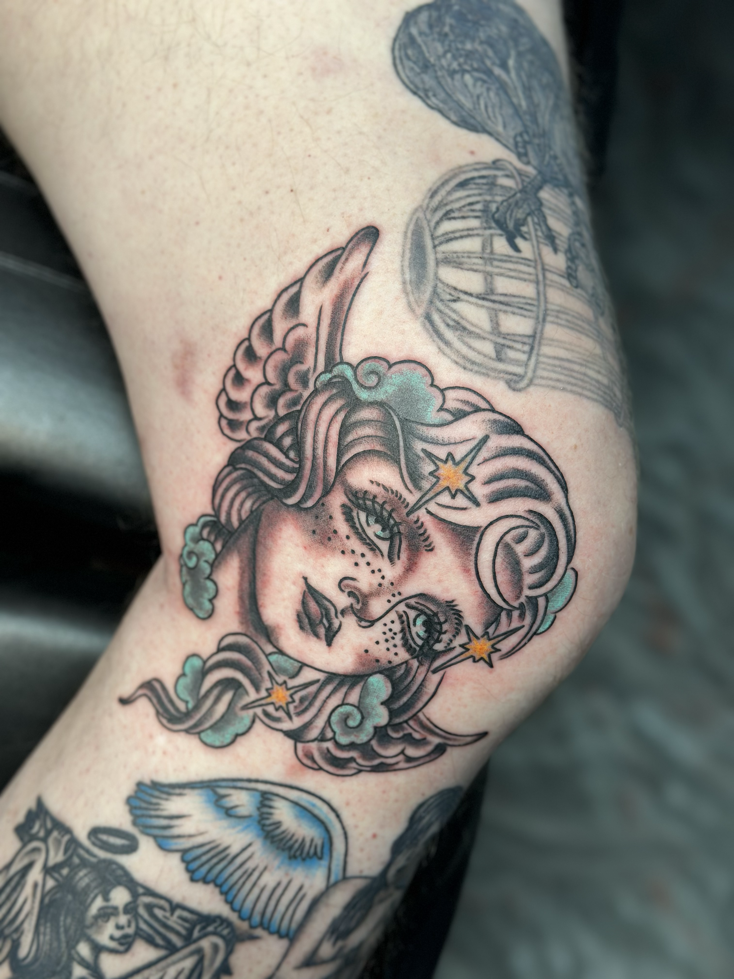 Tattoo of a stylized woman with flowing hair and stars on her face, surrounded by clouds on the upper arm.