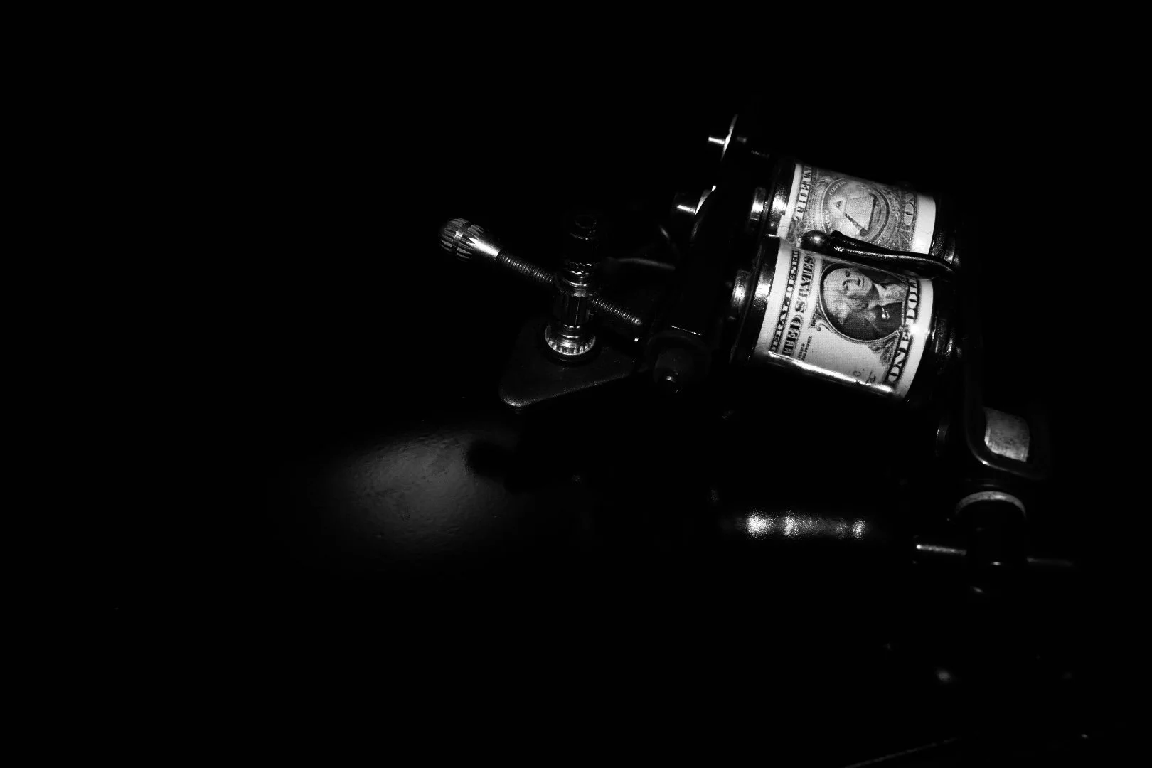 Close-up of a tattoo machine with dollar bills on it, in black and white.