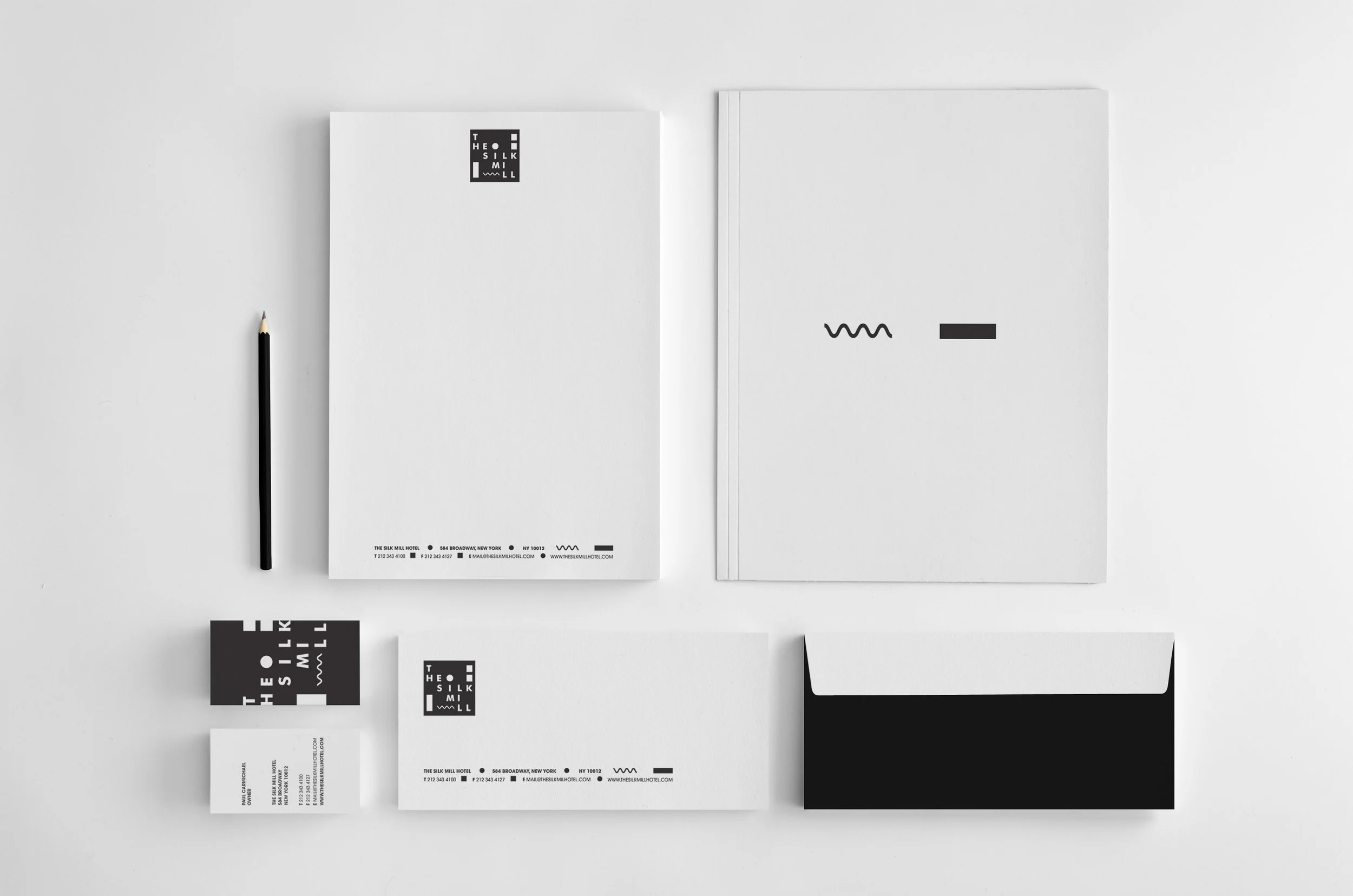 A collection of black and white business stationery including envelopes, letterhead, and business cards with modern minimalistic design on a white surface, alongside a black pencil.