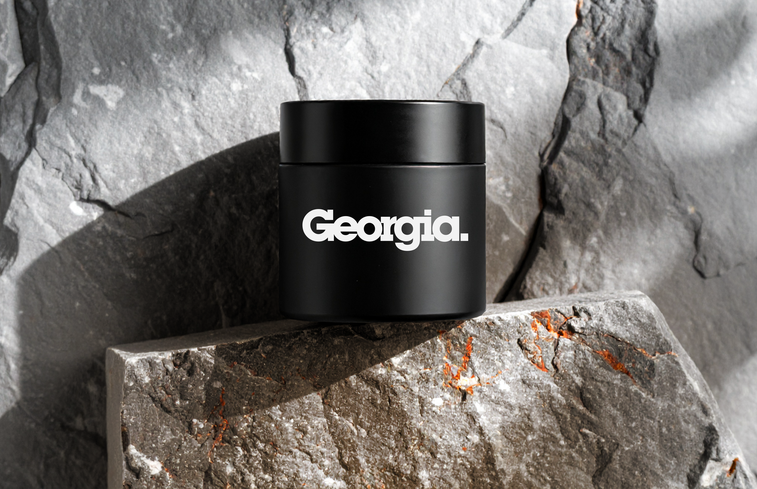 A black container with the word 'Georgia.' in white text, placed on a rough stone surface with a textured stone background.