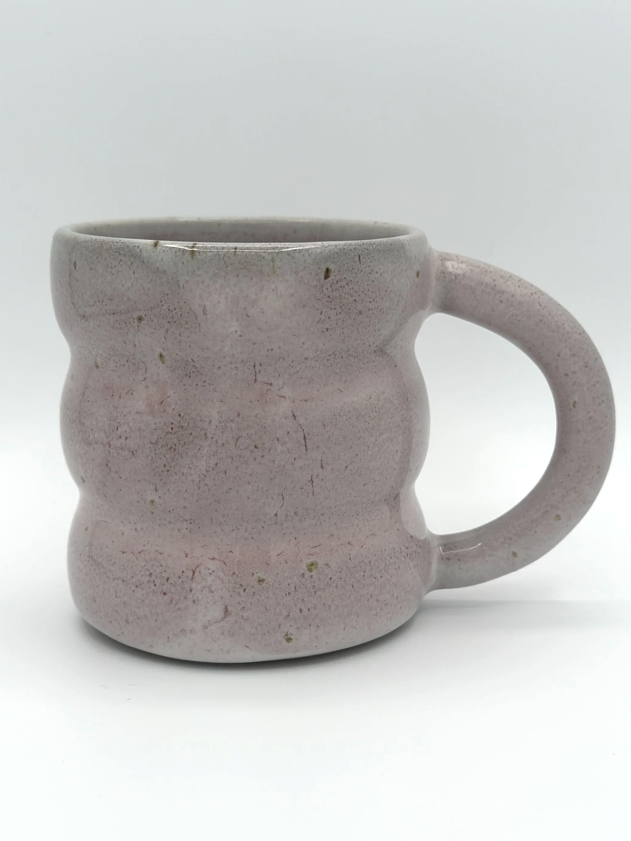 Handmade stoneware mug in matte blush pink with wavy sculpted sides and round handle