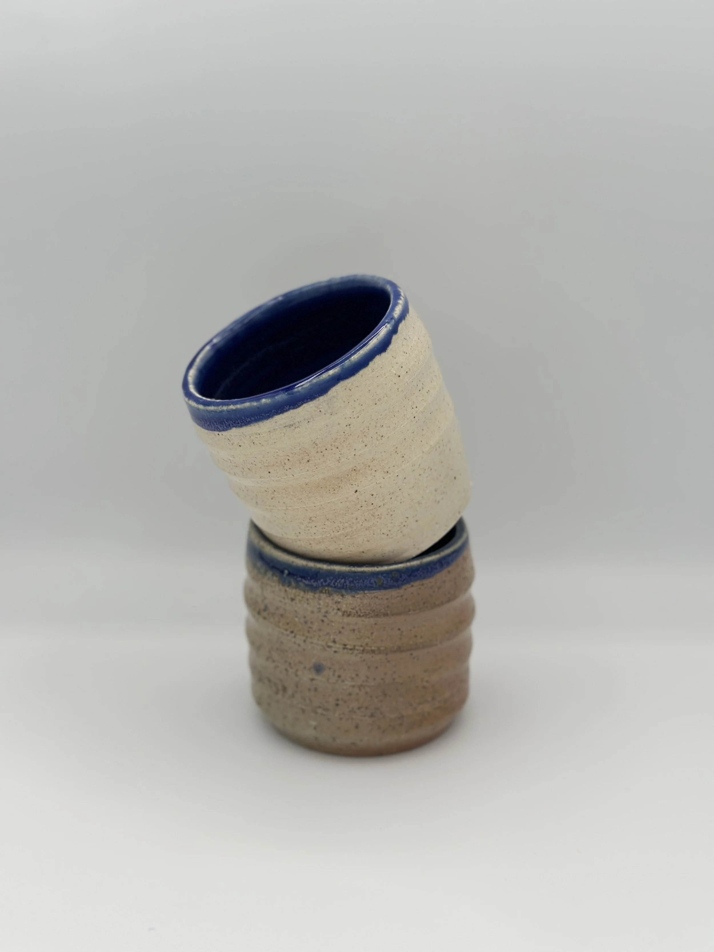 hand holding a pair of swirl cups that have blue rims and atmospheric glossy speckled outsides