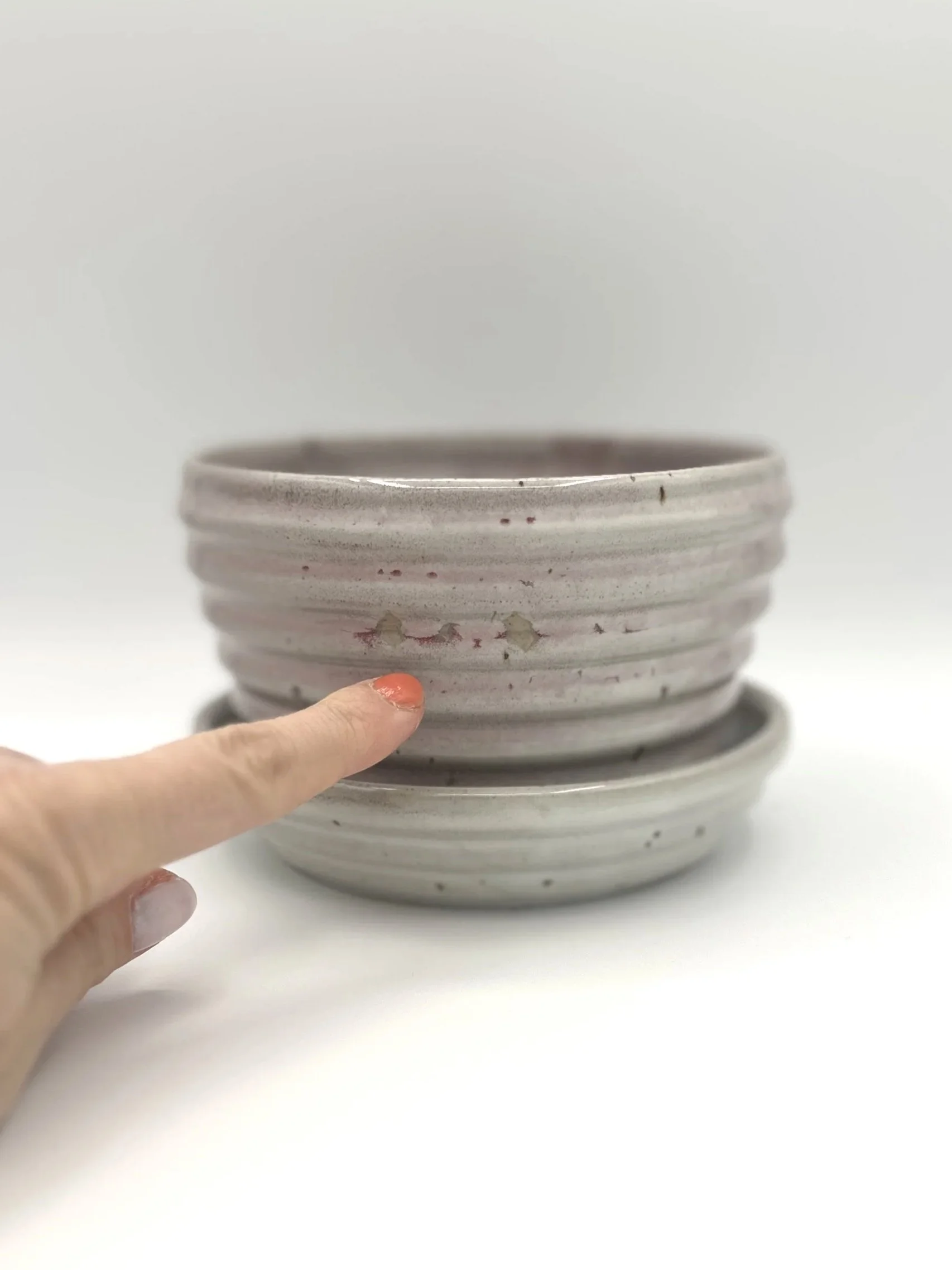 Handmade stoneware ceramic stepped planter and matching stepped tray light pinkish colored shiny candy coated glaze with manicured finger pointing to glaze imperfections