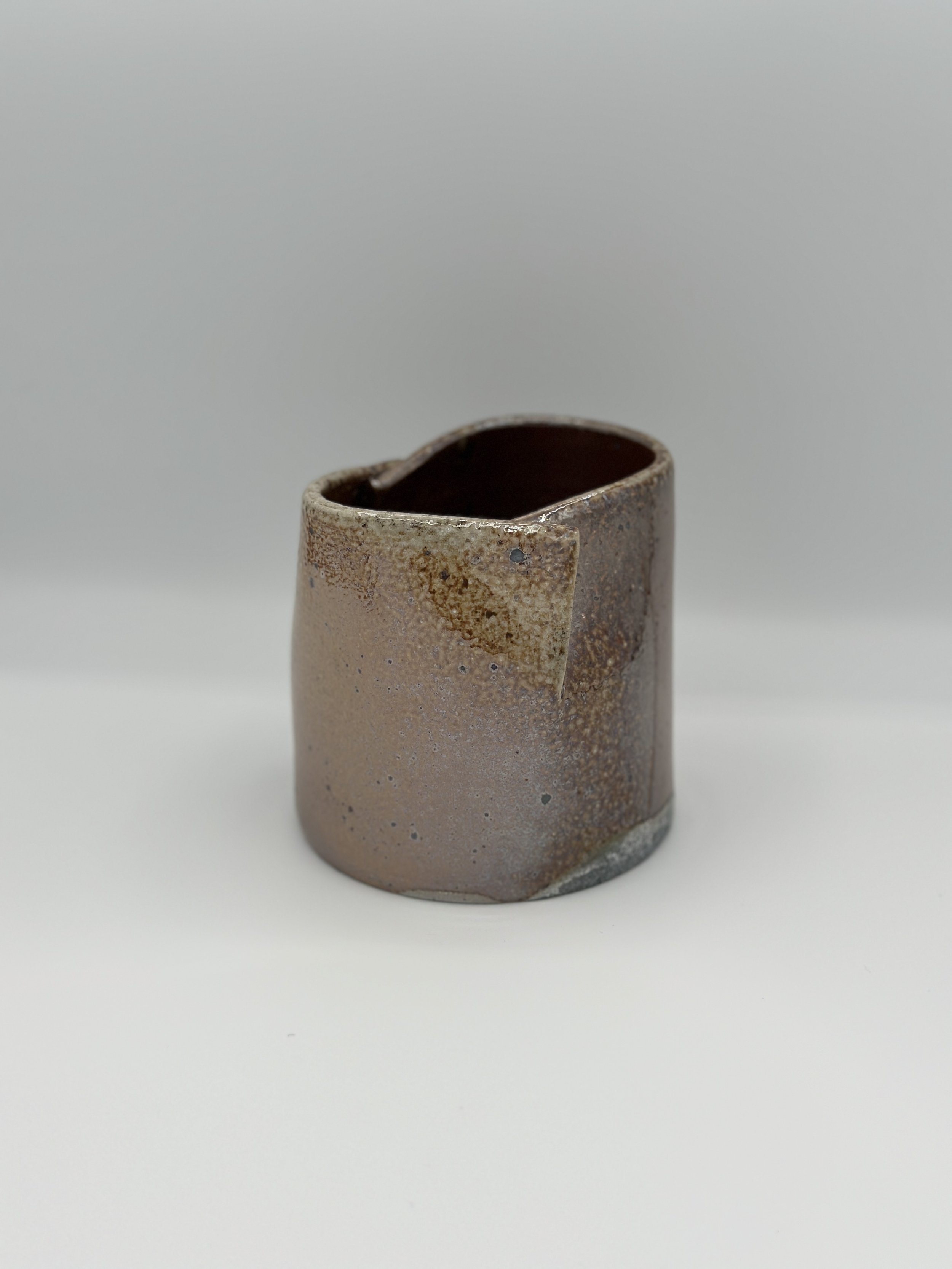 folded shiny metallic ceramic vessel held by a hand with a diagonal modern wood background