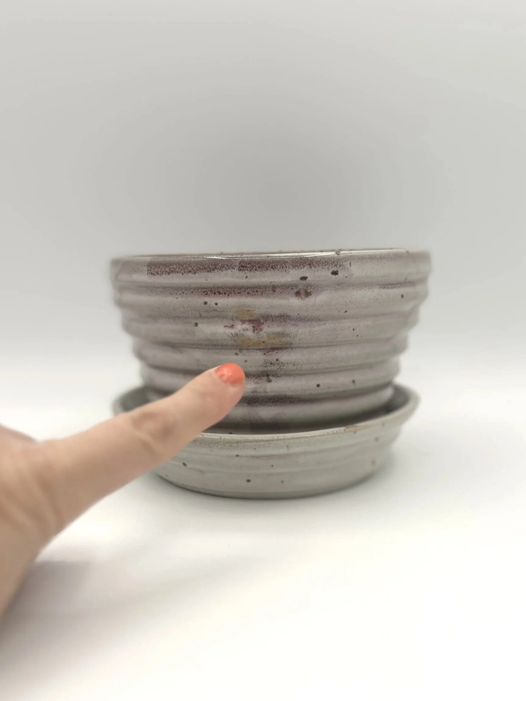 Handmade stoneware ceramic stepped planter and matching stepped tray light pinkish colored shiny candy coated glaze with manicured finger pointing to glaze imperfections