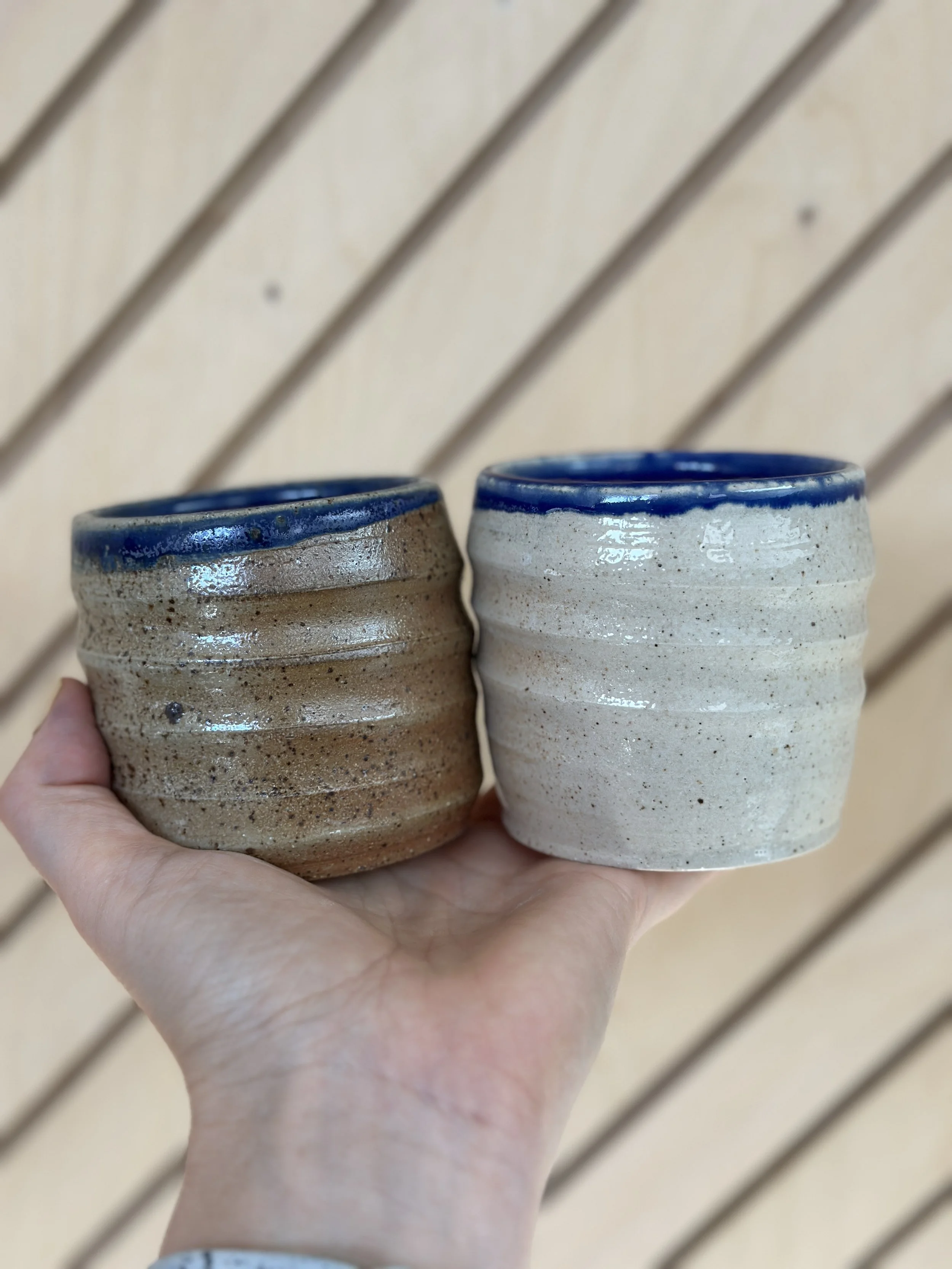 hand holding a pair of swirl cups that have blue rims and atmospheric glossy speckled outsides