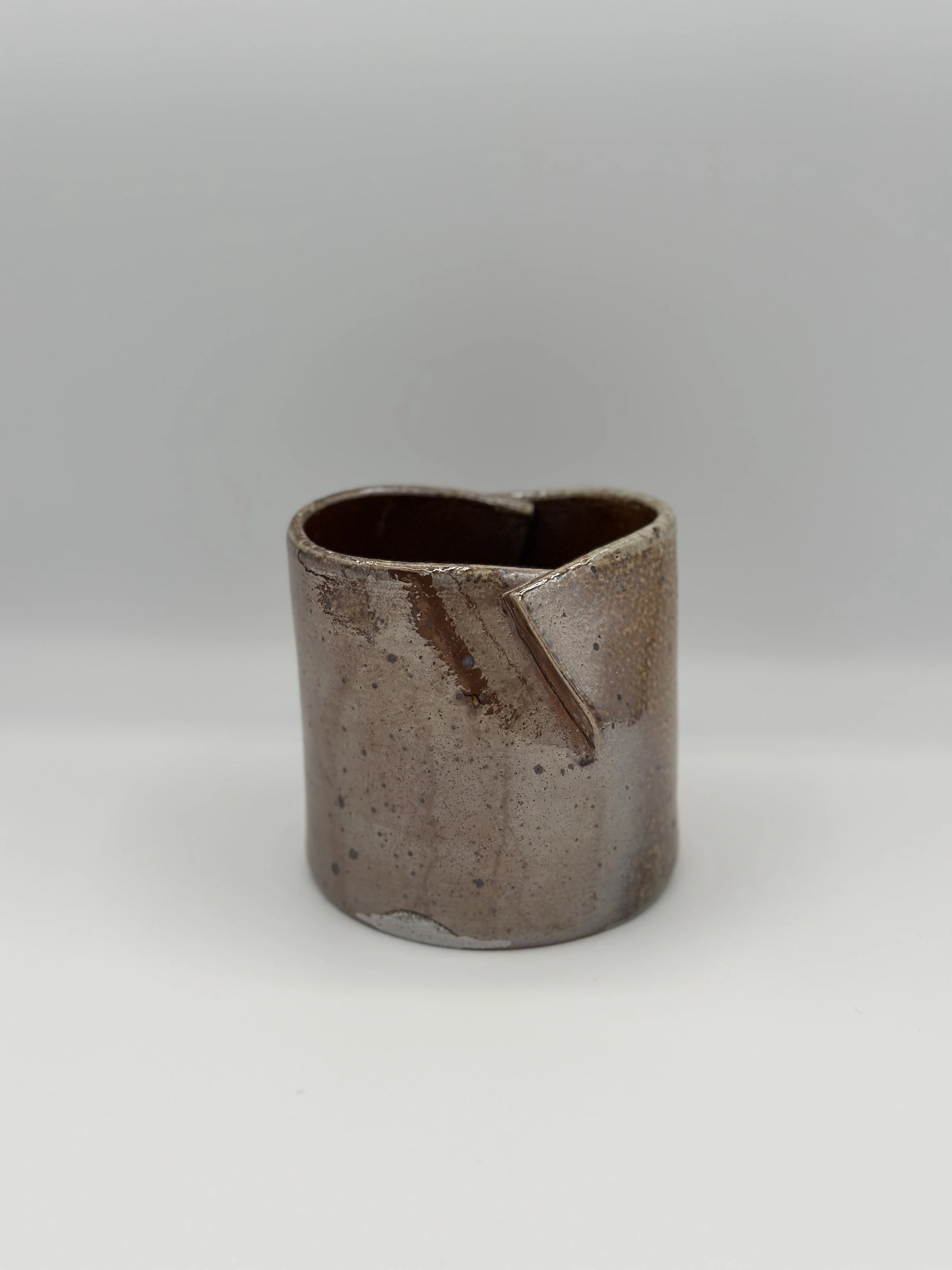 folded shiny metallic ceramic vessel held by a hand with a diagonal modern wood background