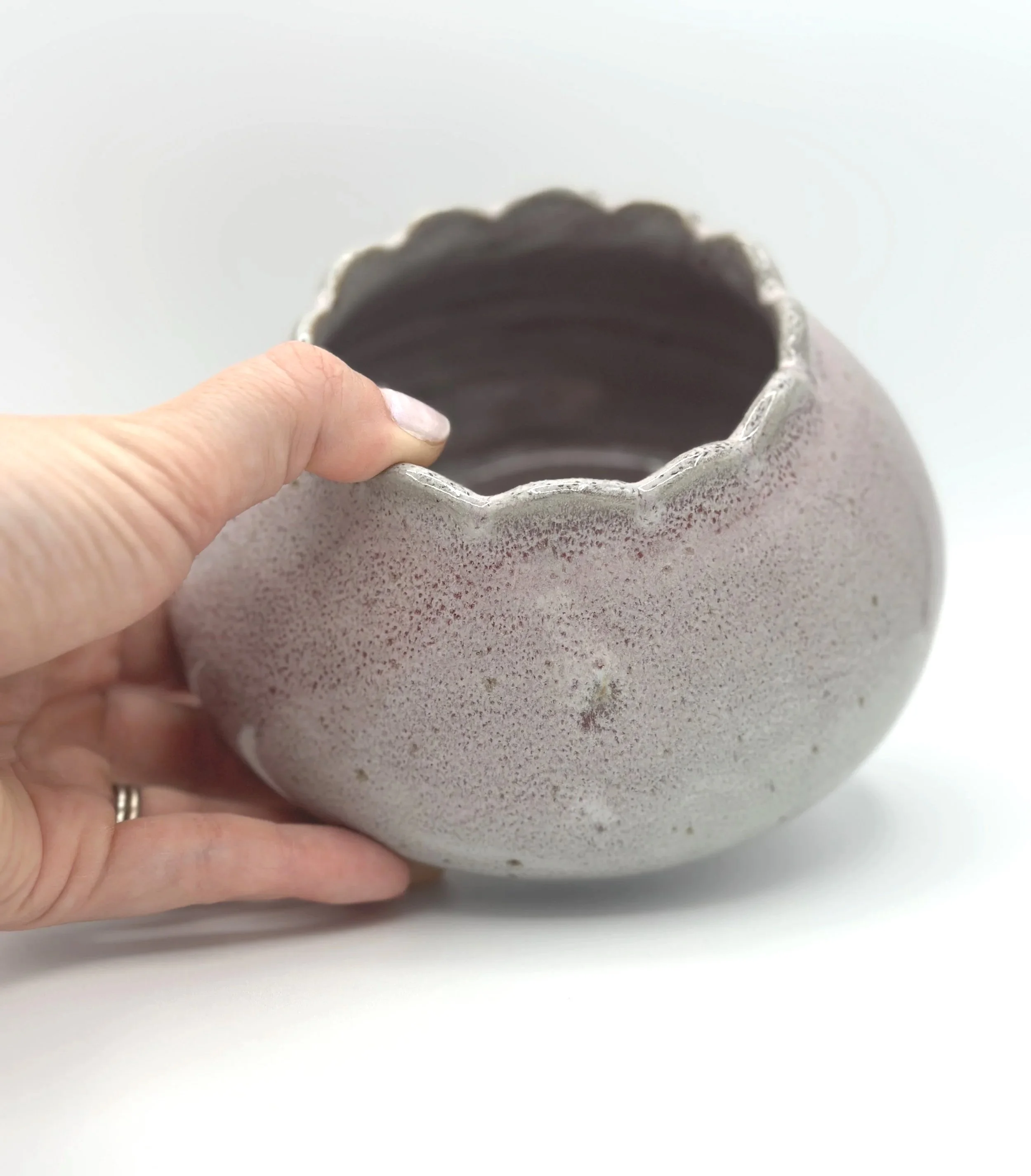 handmade stoneware ceramic bud vase in glossy lavender, mauve, pink and grey glaze with scalloped rims held by a manicured hand