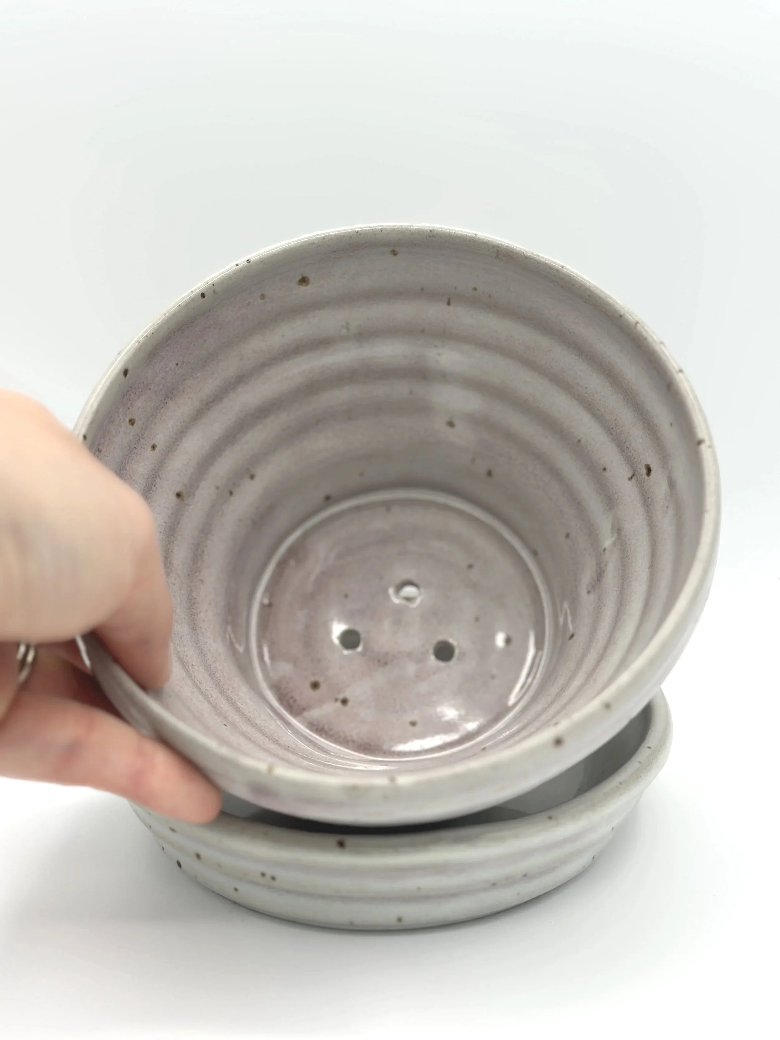 handmade stoneware ceramic planter with ribbed texture and tray. color is a deep mix of grey and pink with lots of motion and variability held by a manicured hand to show it off on its side