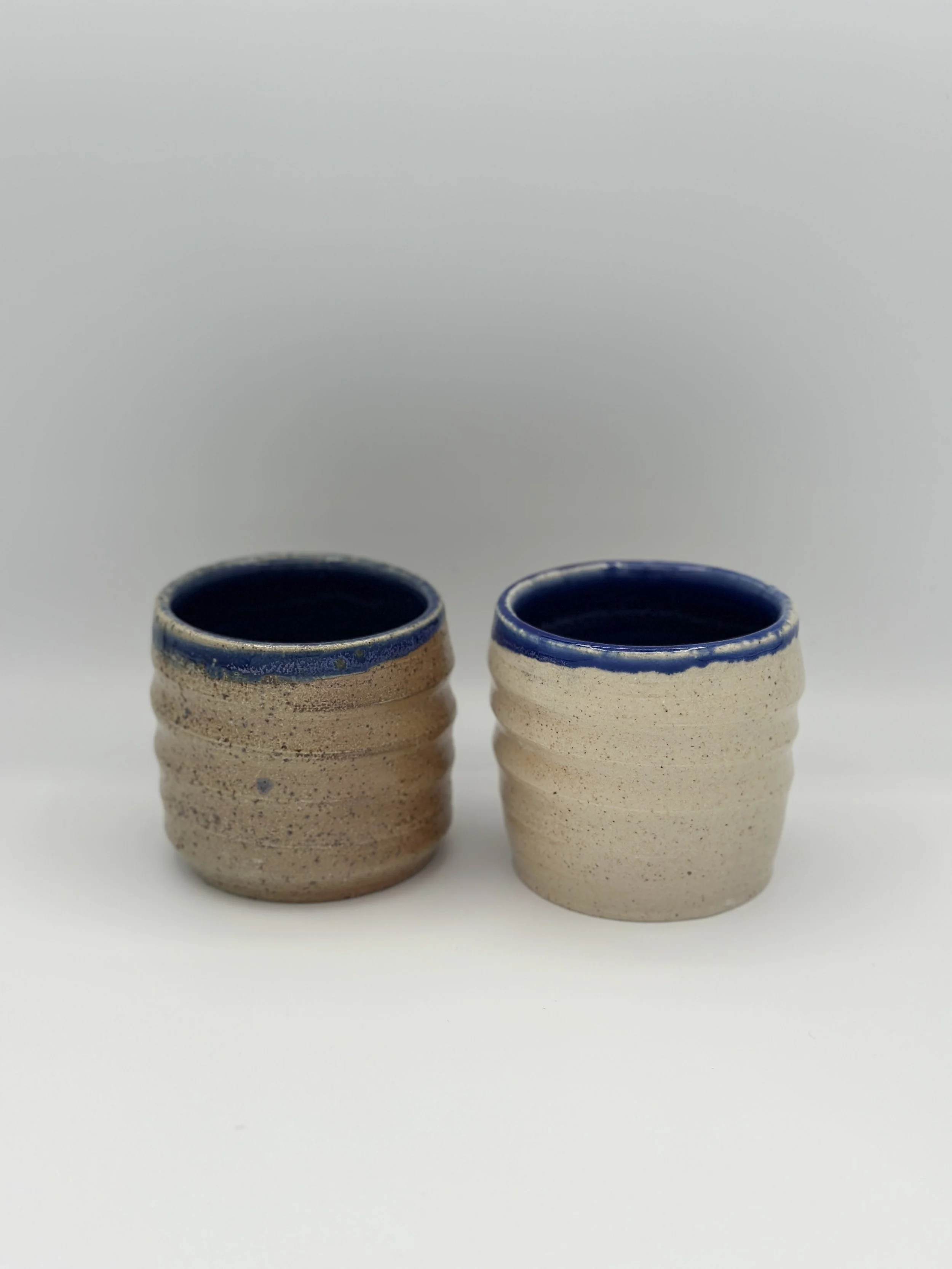 hand holding a pair of swirl cups that have blue rims and atmospheric glossy speckled outsides