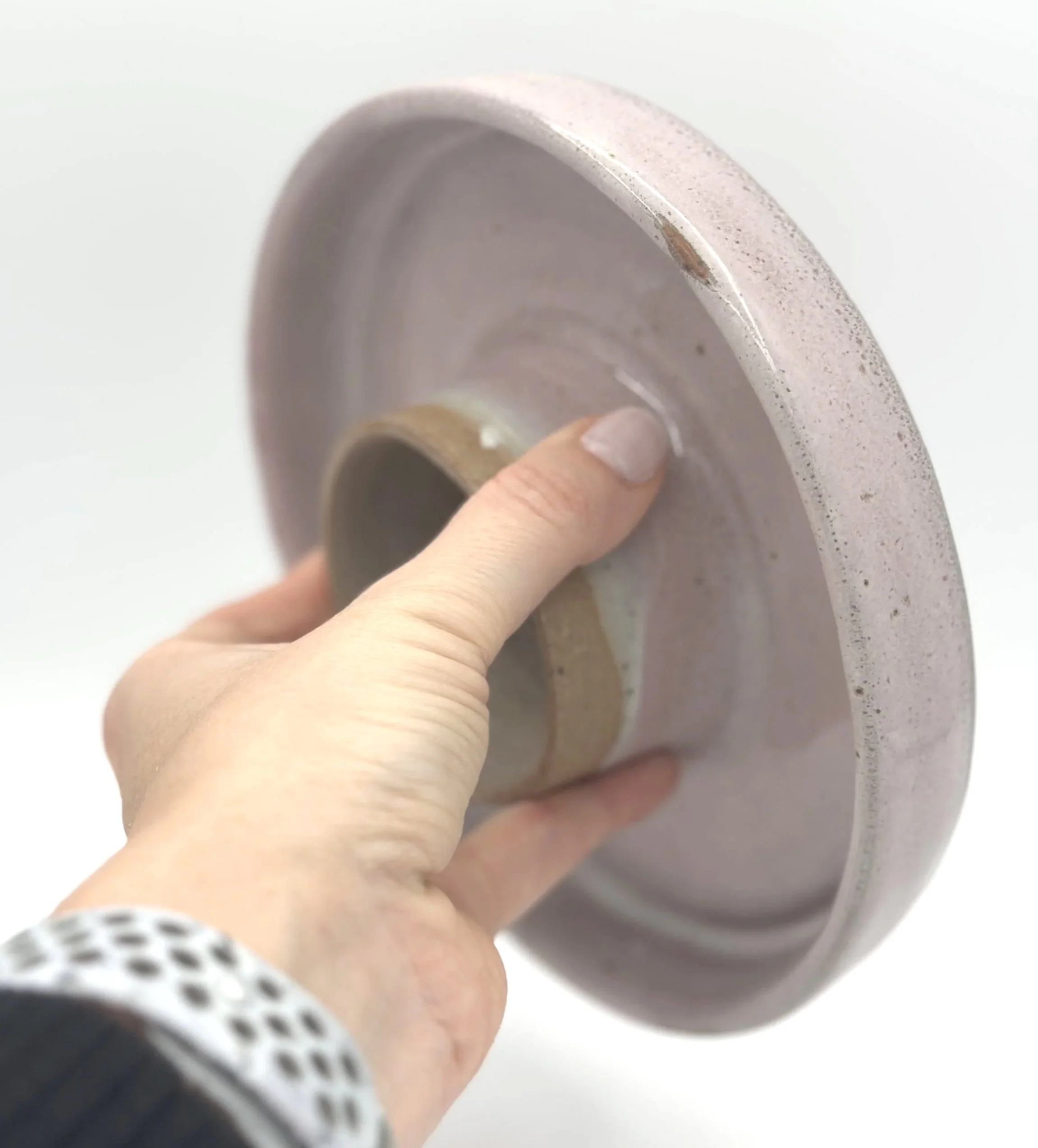 handmade stoneware ceramic cake stand with pink speckled glaze held by the bottom in a hand showing off the small unglazed stem