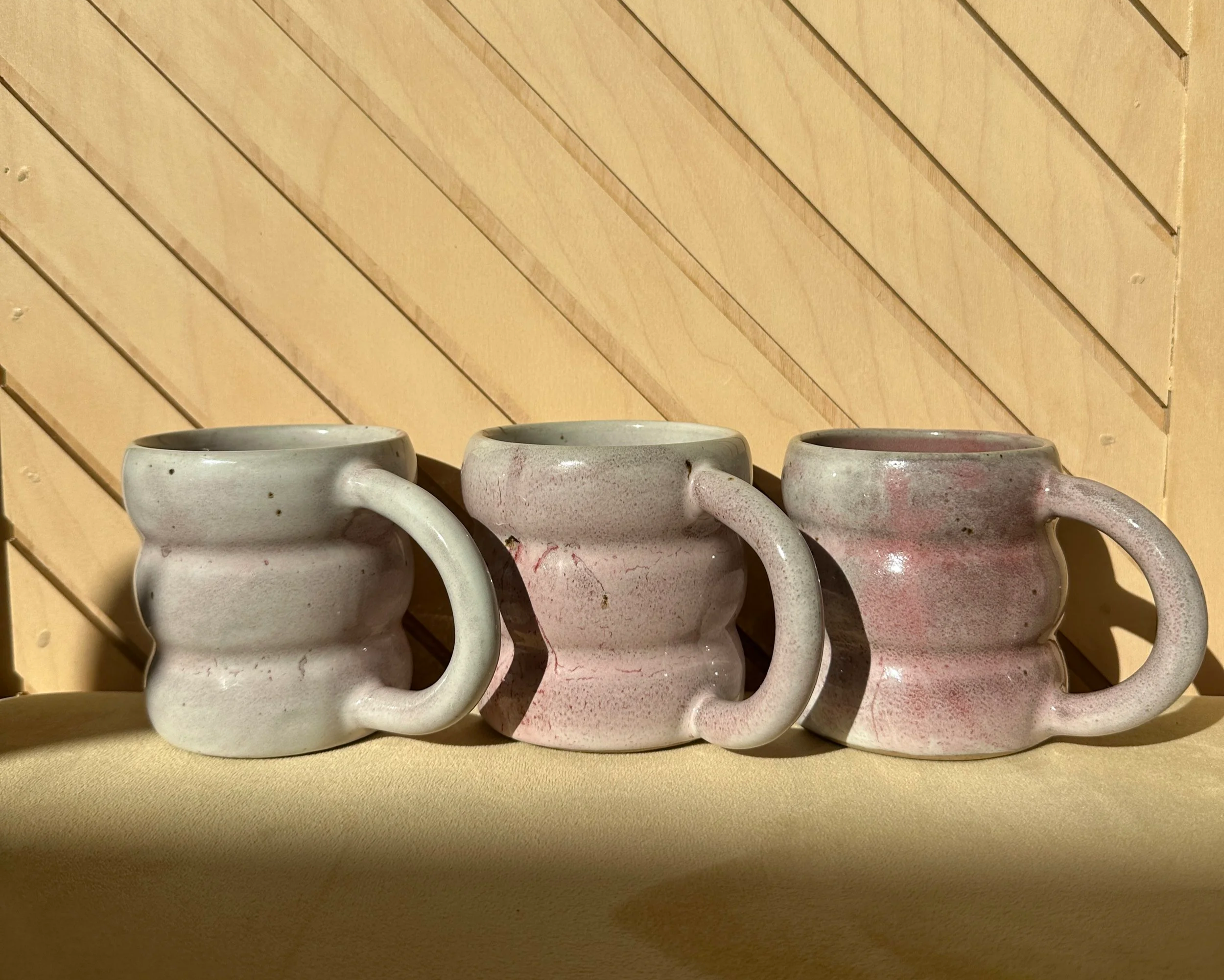 Three handmade stoneware cups, grey glaze with pink blush speckles, rippled texture