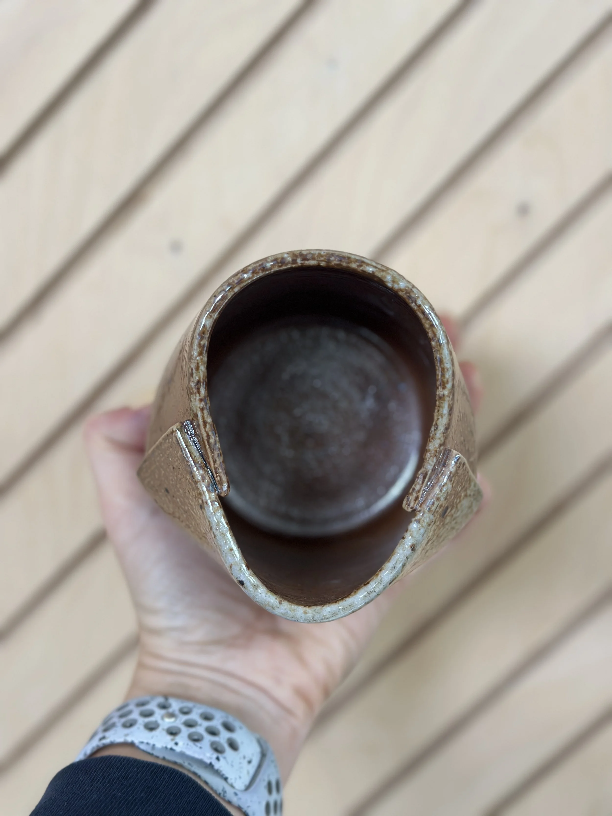 folded shiny metallic ceramic vessel held by a hand with a diagonal modern wood background
