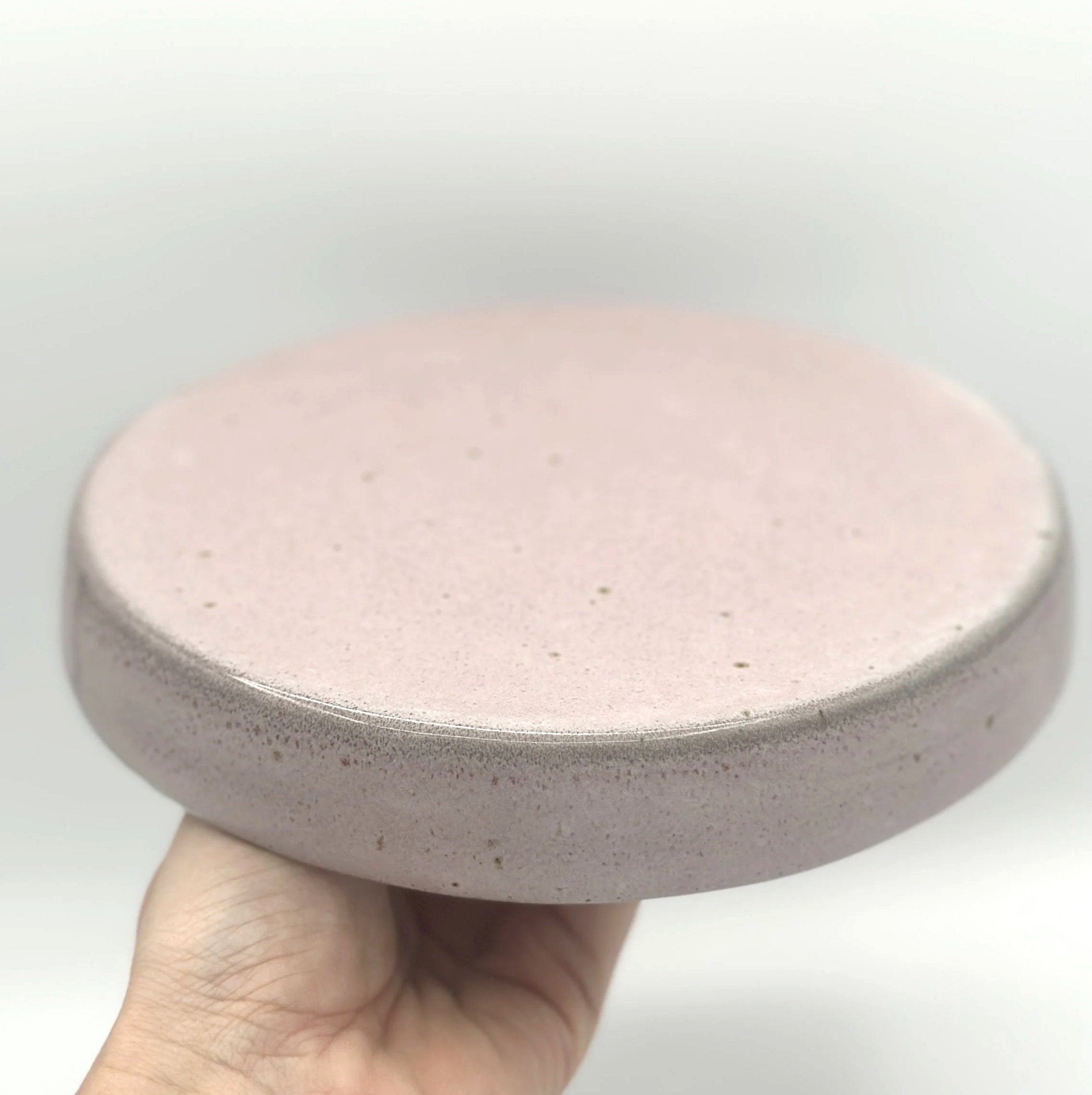 handmade stoneware ceramic cake stand with pink speckled glaze held by the bottom in a hand