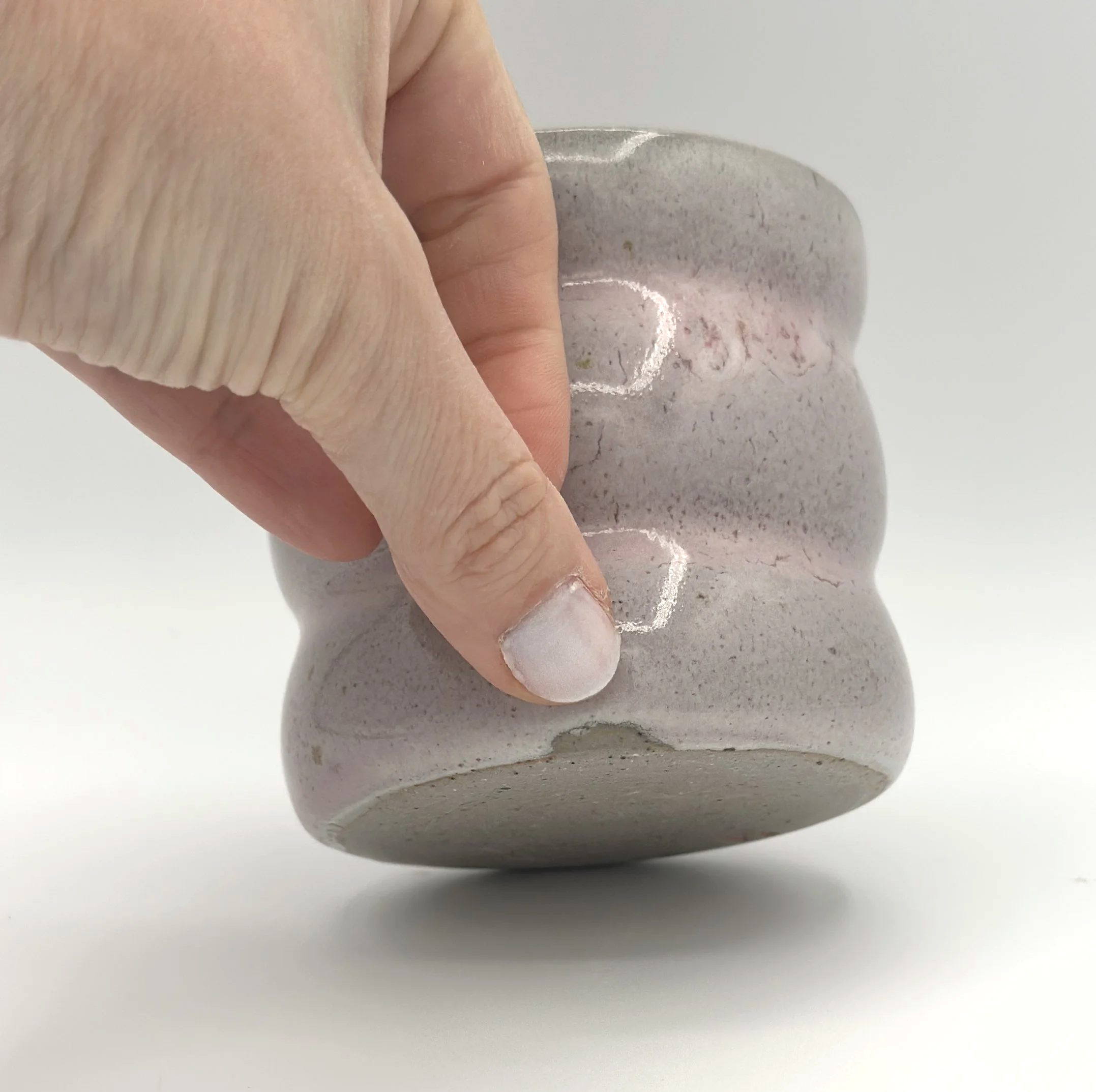 Handmade stoneware ceramic tumbler with 3 bubbles in modern grey slightly blushed colored shiny candy coated glaze with manicured fingers pointing out glaze imperfection