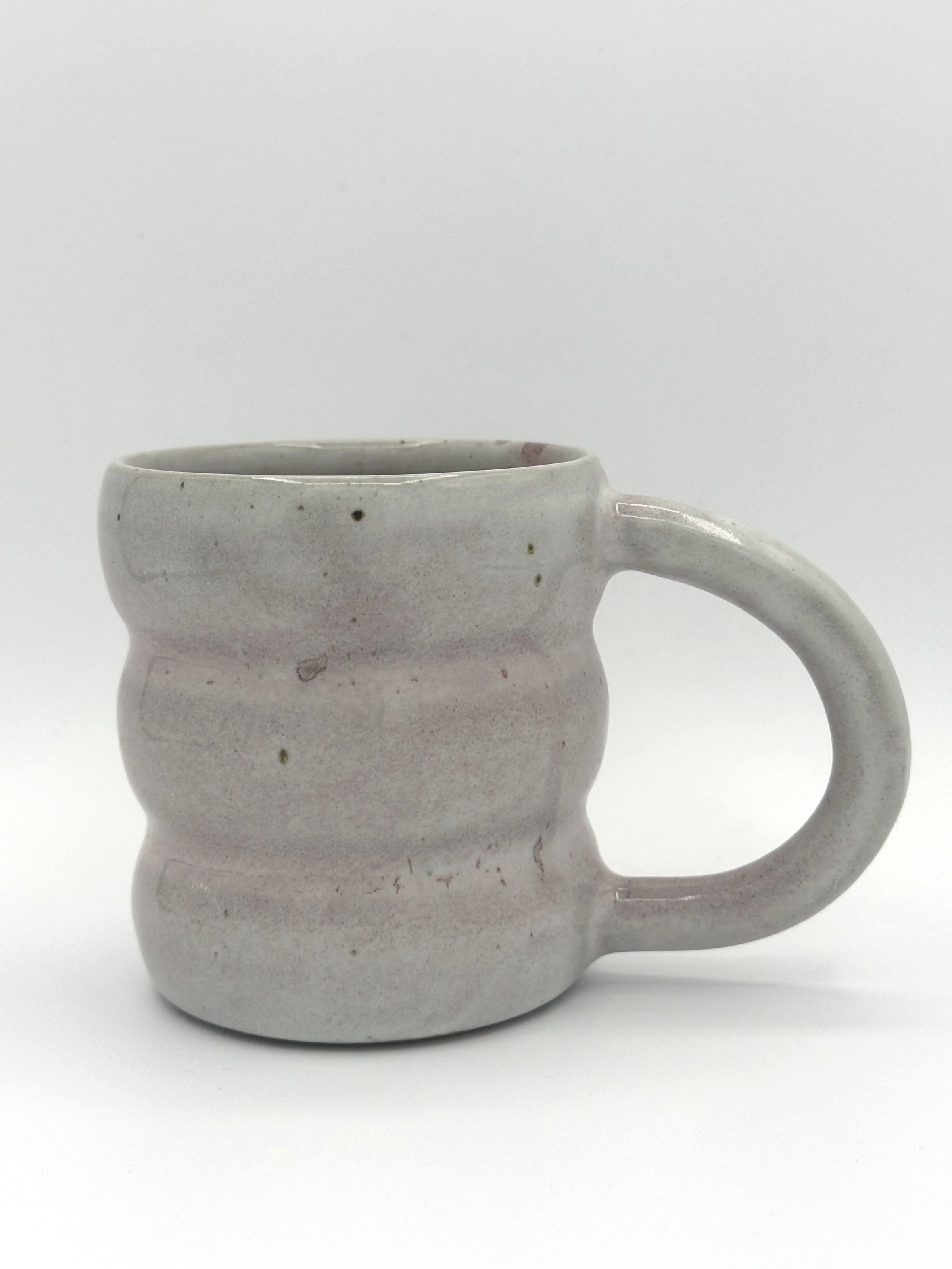 Handmade stoneware mug in matte blush pink with wavy sculpted sides and round handle