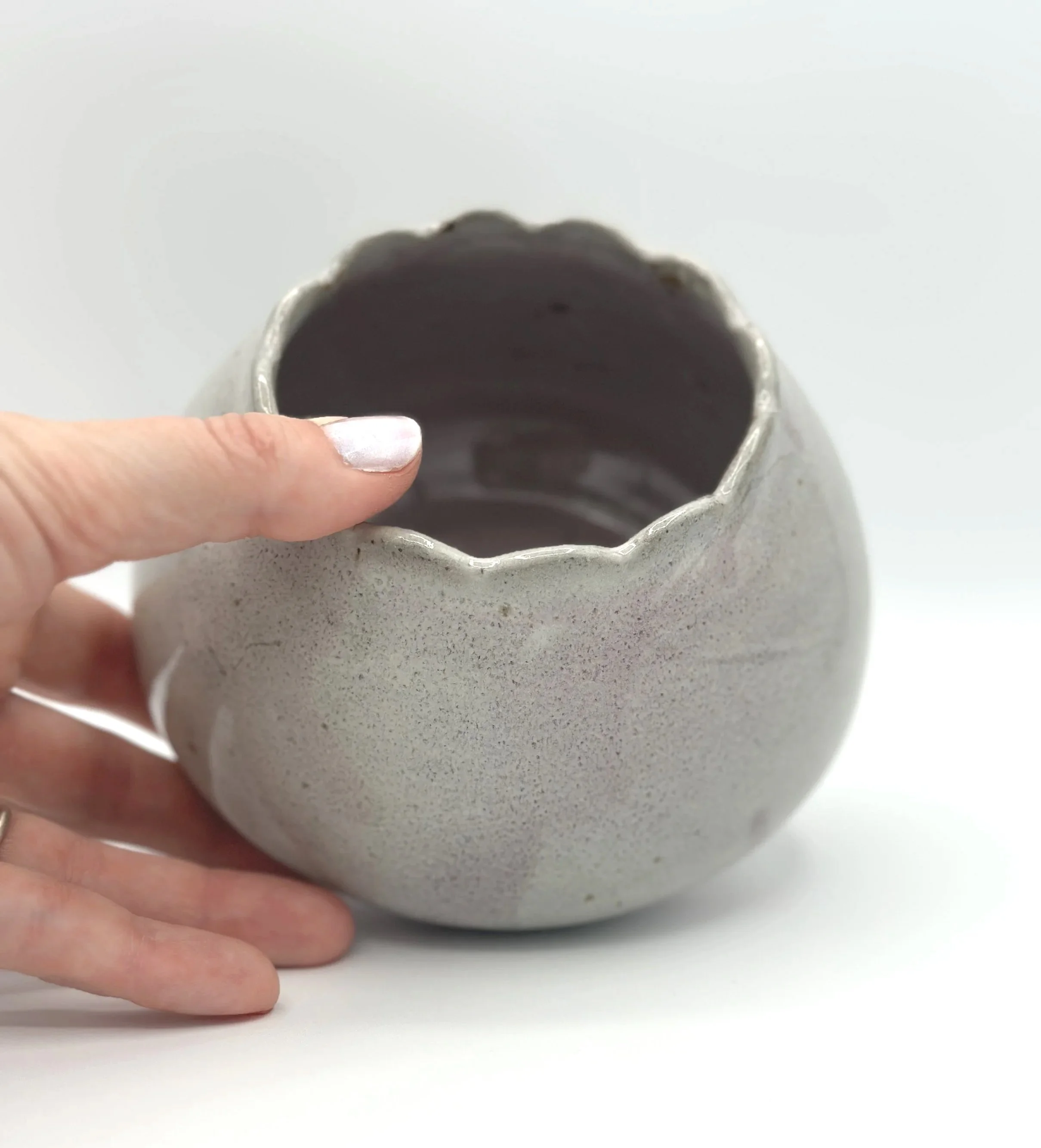 handmade stoneware ceramic bud vase in glossy lavender, mauve, pink and grey glaze with scalloped rims held by a manicured hand