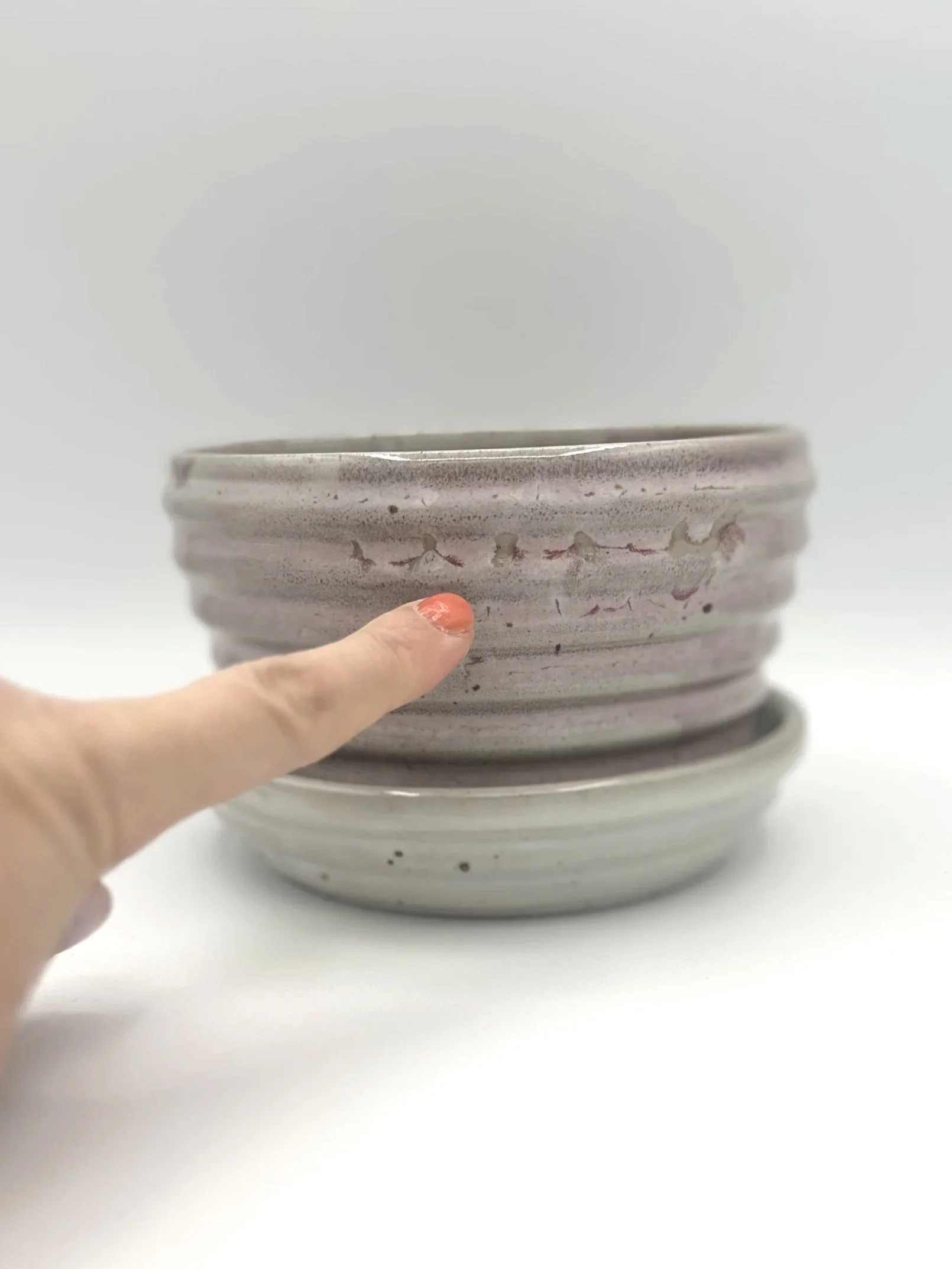 Handmade stoneware ceramic stepped planter and matching stepped tray light pinkish colored shiny candy coated glaze with manicured finger pointing to glaze imperfections