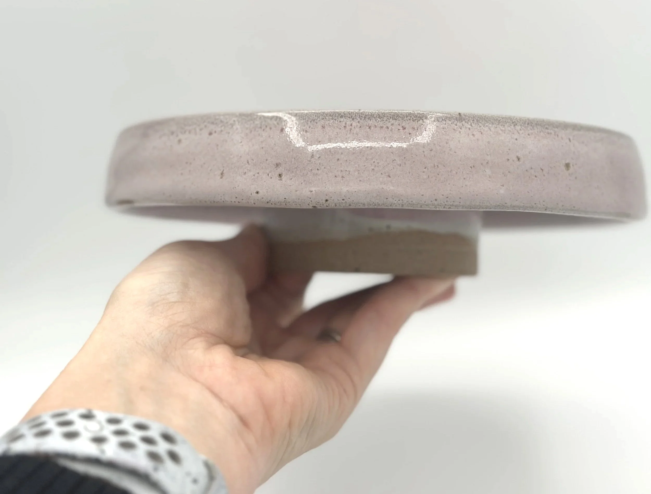 handmade stoneware ceramic cake stand with pink speckled glaze held by the bottom in a hand