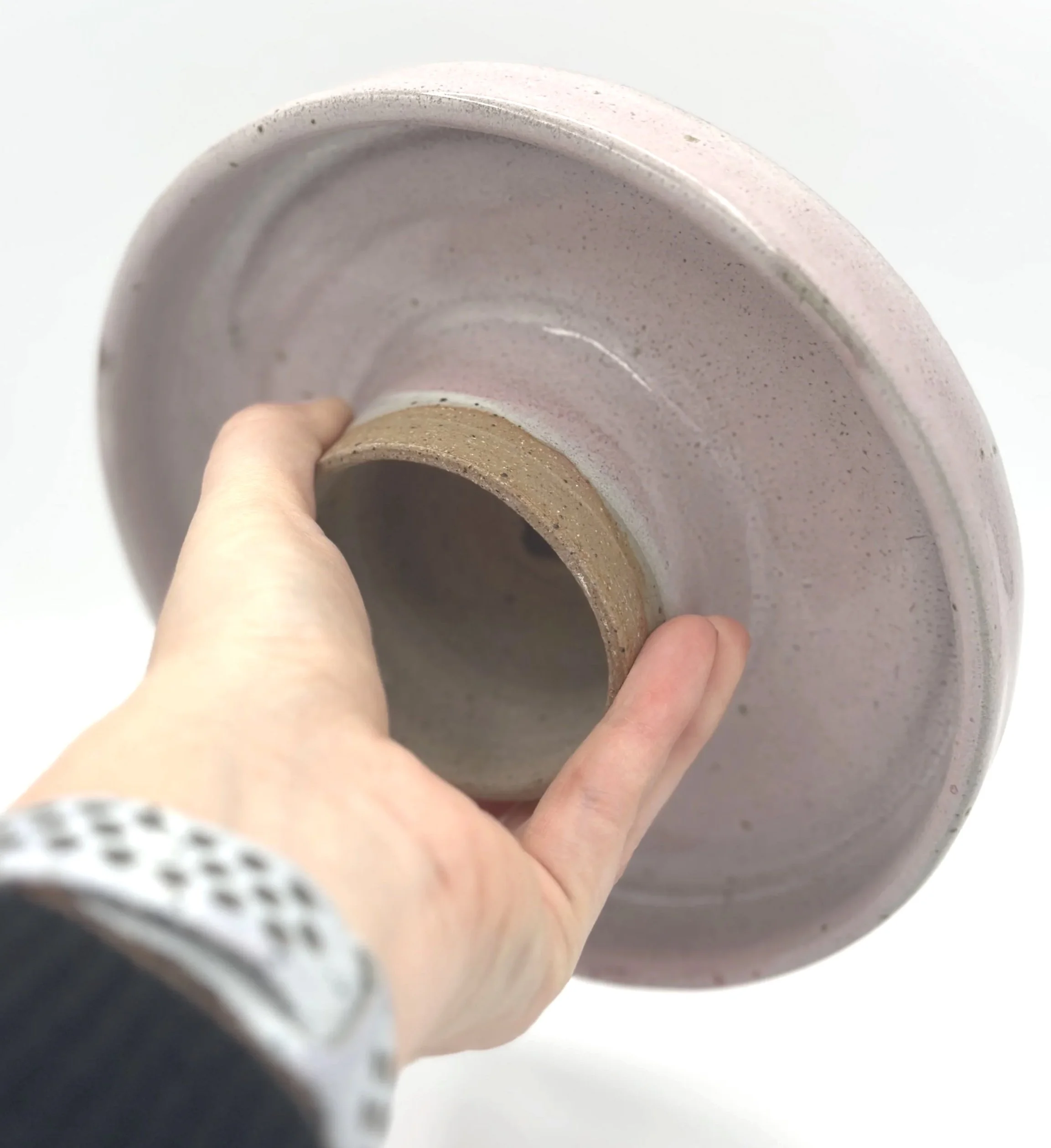 handmade stoneware ceramic cake stand with pink speckled glaze held by the bottom in a hand showing off the small unglazed stem