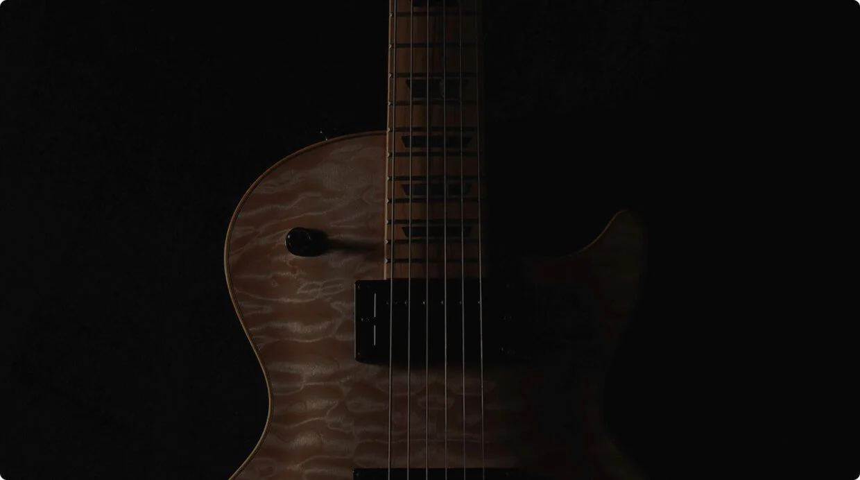 Close-up of a semi-hollow electric guitar with a quilted maple top against a black background.