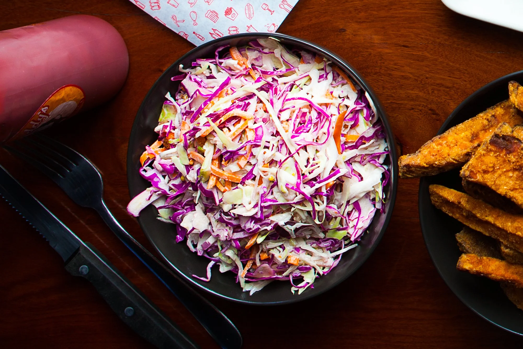 A black bowl filled with coleslaw salad containing shredded purple and green cabbage, and carrots, placed on a wooden table.