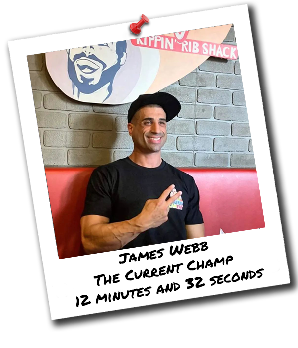 Man sitting in a diner booth with brick wall background, wearing a black t-shirt and black cap, smiling and making a peace sign.  Photo caption: 'James Webb, the current champ, 12 minutes and 32 seconds.' Hungry Horn Challenge Winner at Big Roddy's.