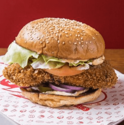 Fried chicken burger sandwich with lettuce, tomato, onion, and pickles on a sesame seed bun.