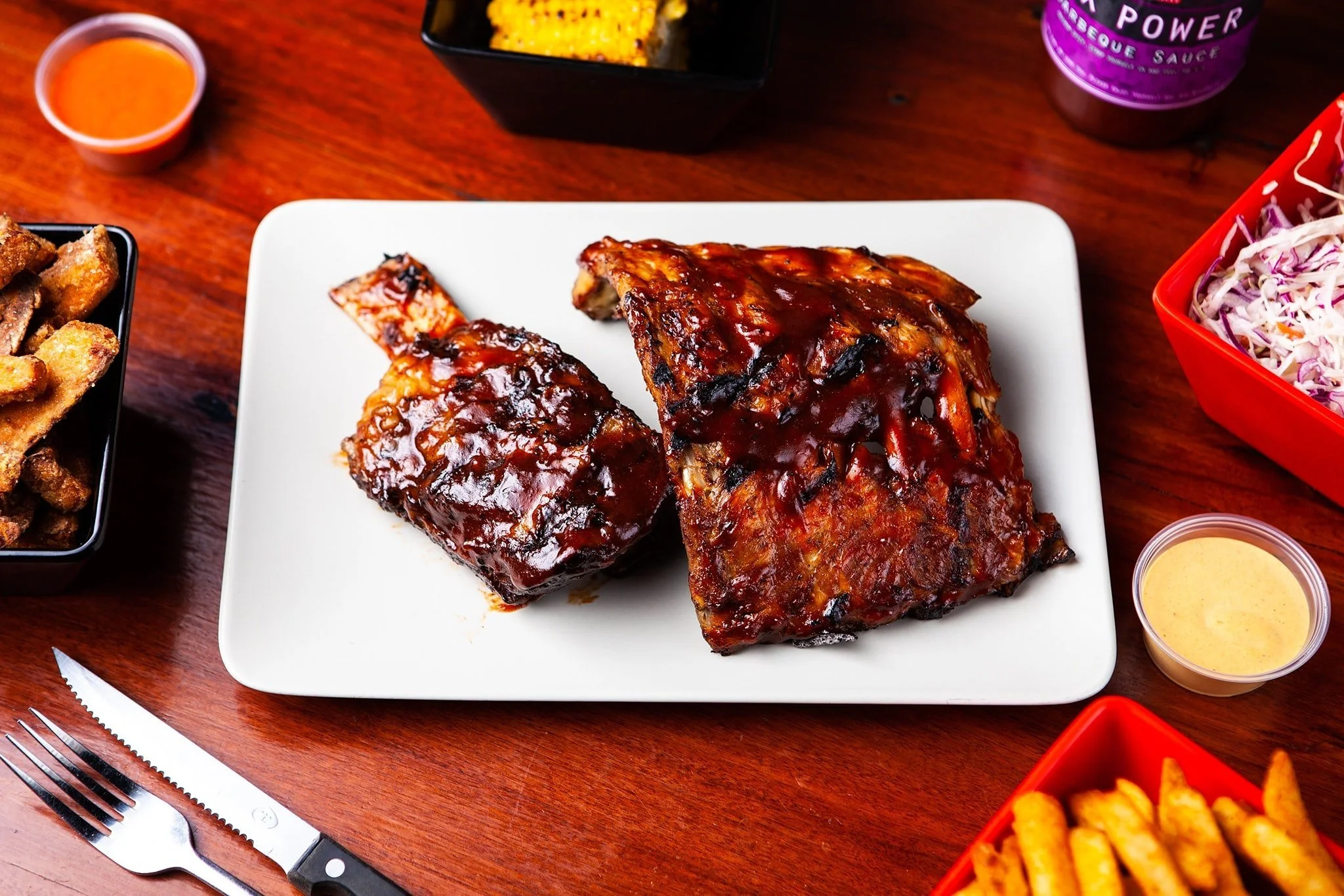 Barbecue pork ribs on a white plate with side dishes on a wooden table.