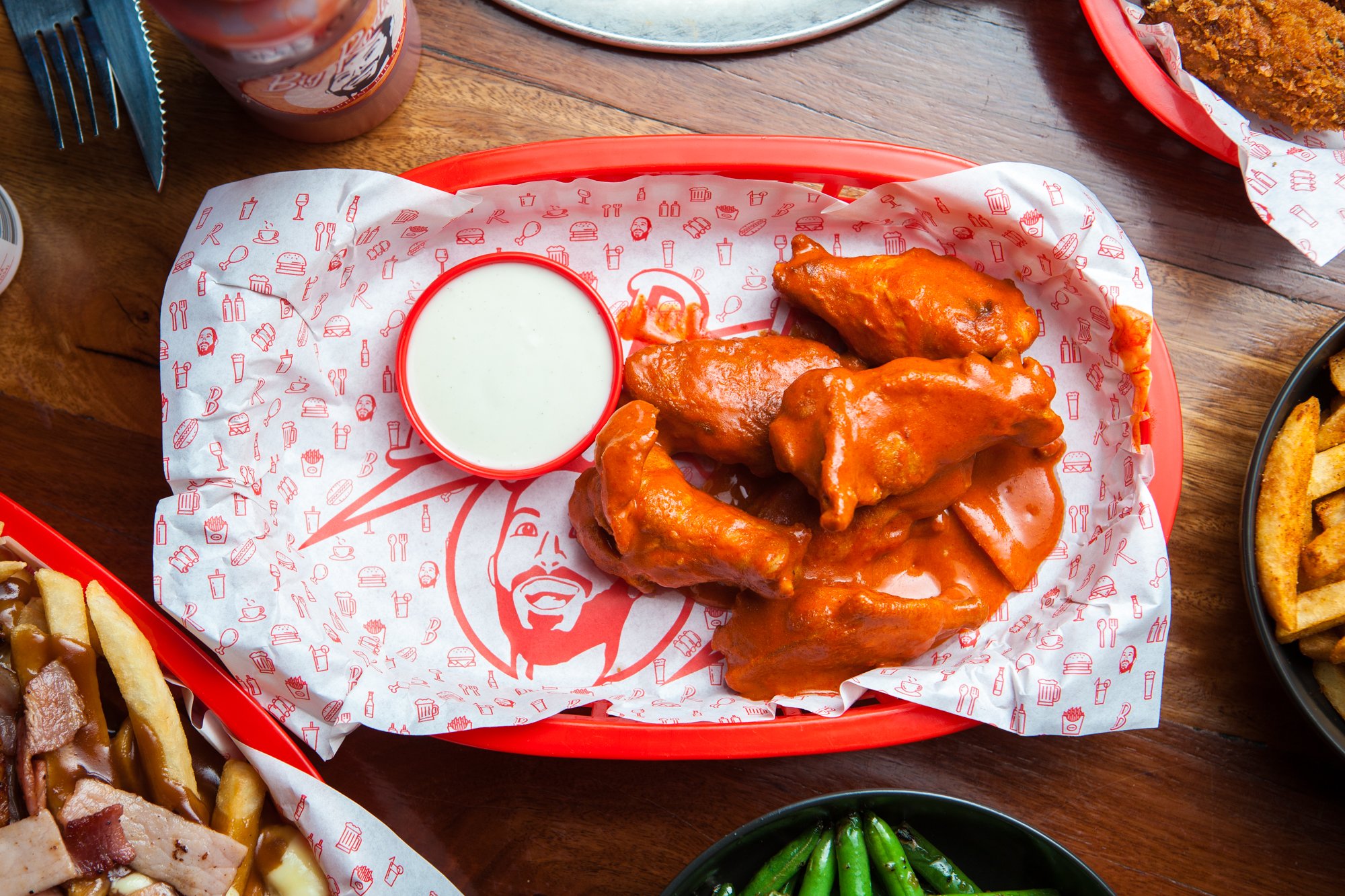 Basket of chicken wings coated in hot sauce with a side of ranch dressing.