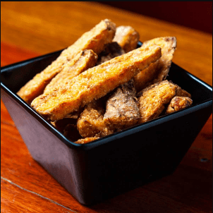 A black square bowl filled with fried chicken tenders on a wooden table.