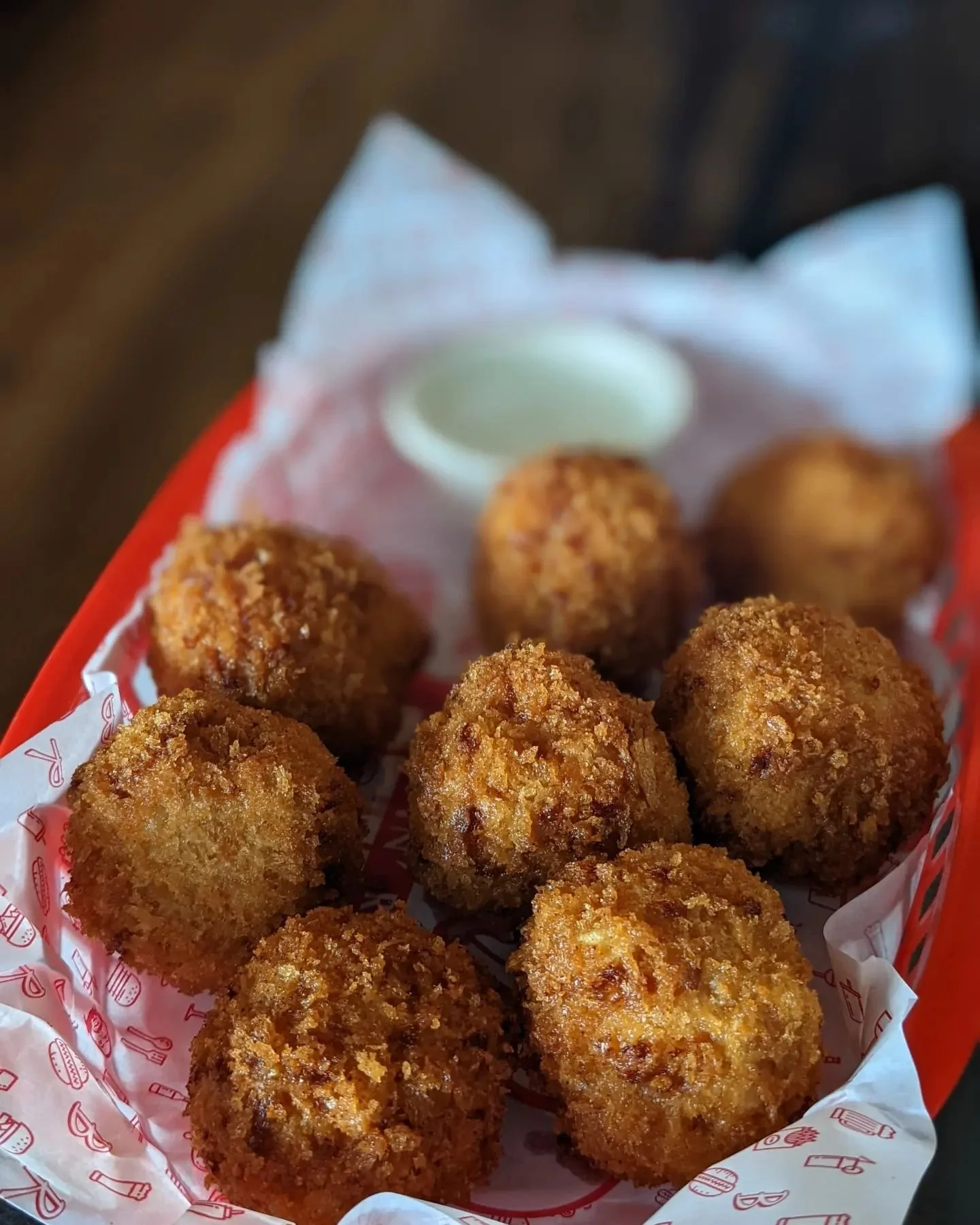 Crispy deep fried mac and cheese balls/ bites/ arancini with dipping sauce in a red basket. 