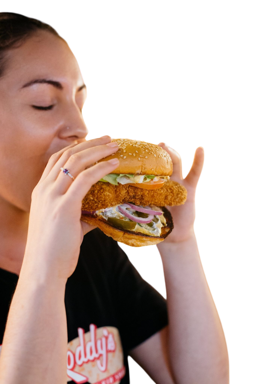 Woman holding a large burger sandwich layered with fried chicken, lettuce, tomato, and pickles.