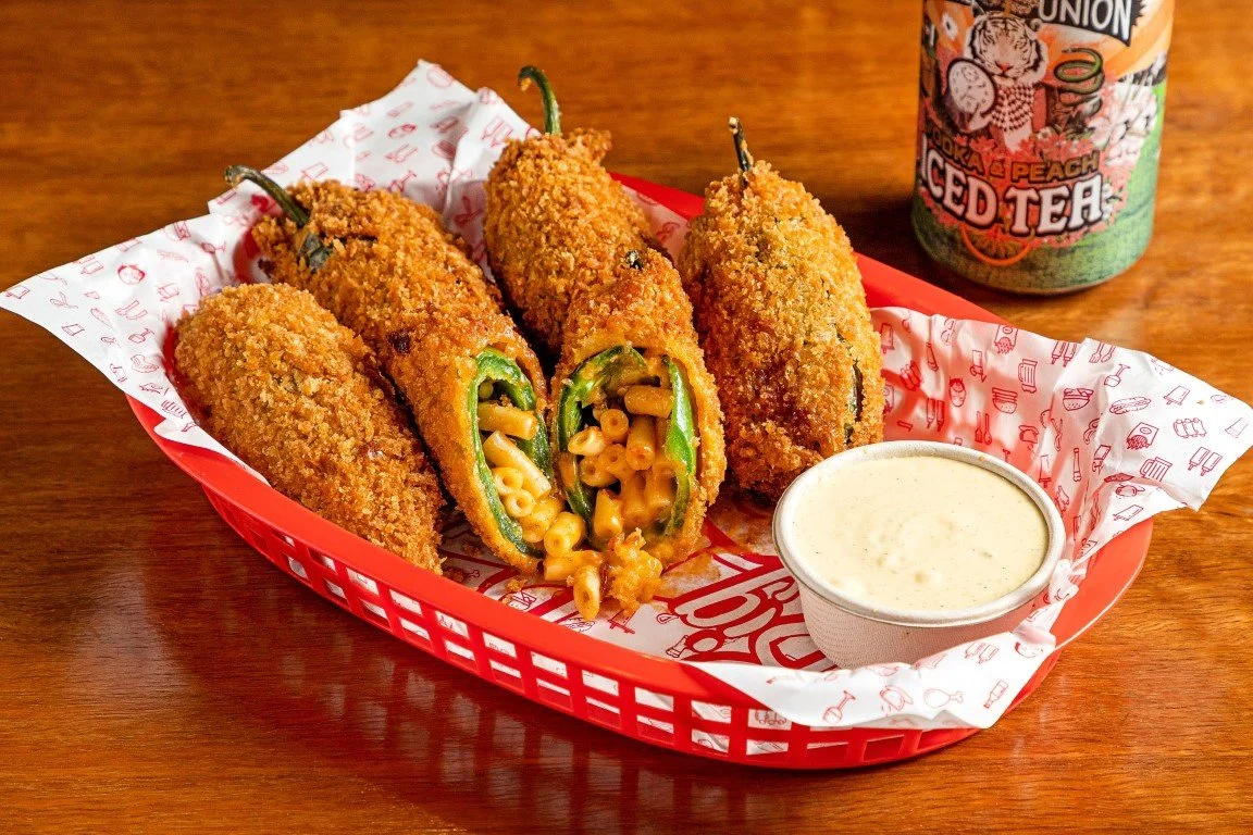 Fried stuffed jalapeño peppers filled with macaroni and cheese, served with a side of creamy dipping sauce, and a can of peach-flavored iced tea in the background (and ginger beer).