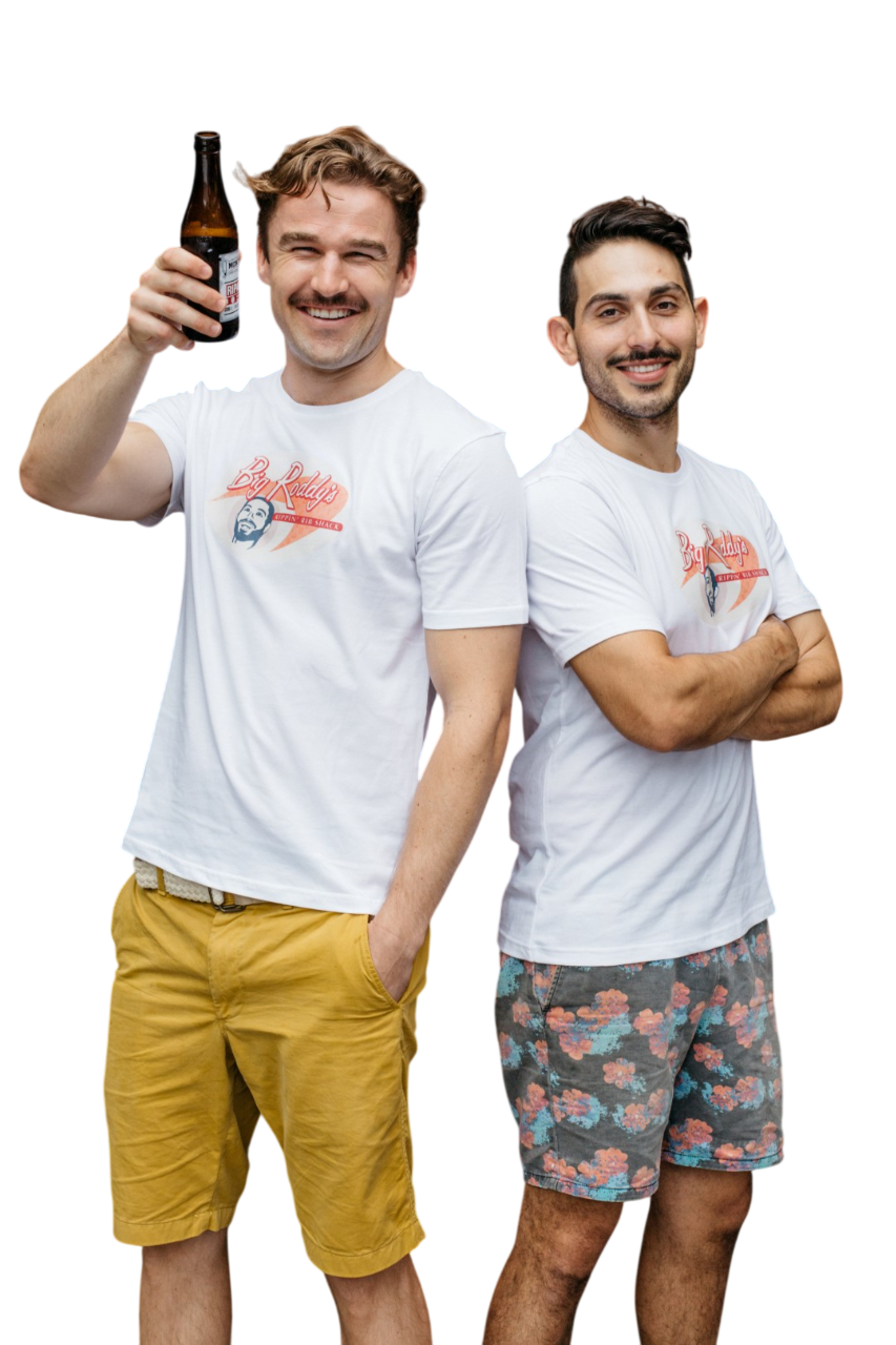 Two smiling young men (Roderick Saba and David Kempnich) in casual summer clothing, one holding a beer bottle, standing close together against a black background. Best friends.