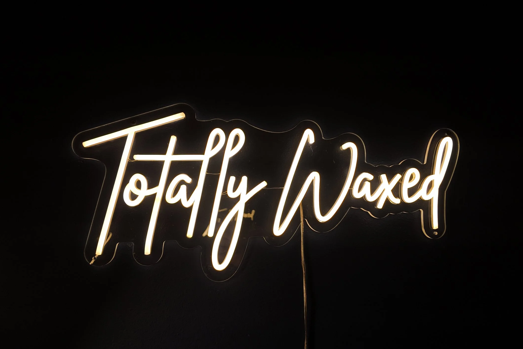 Neon sign reading 'Totally Waxed' against a black background.