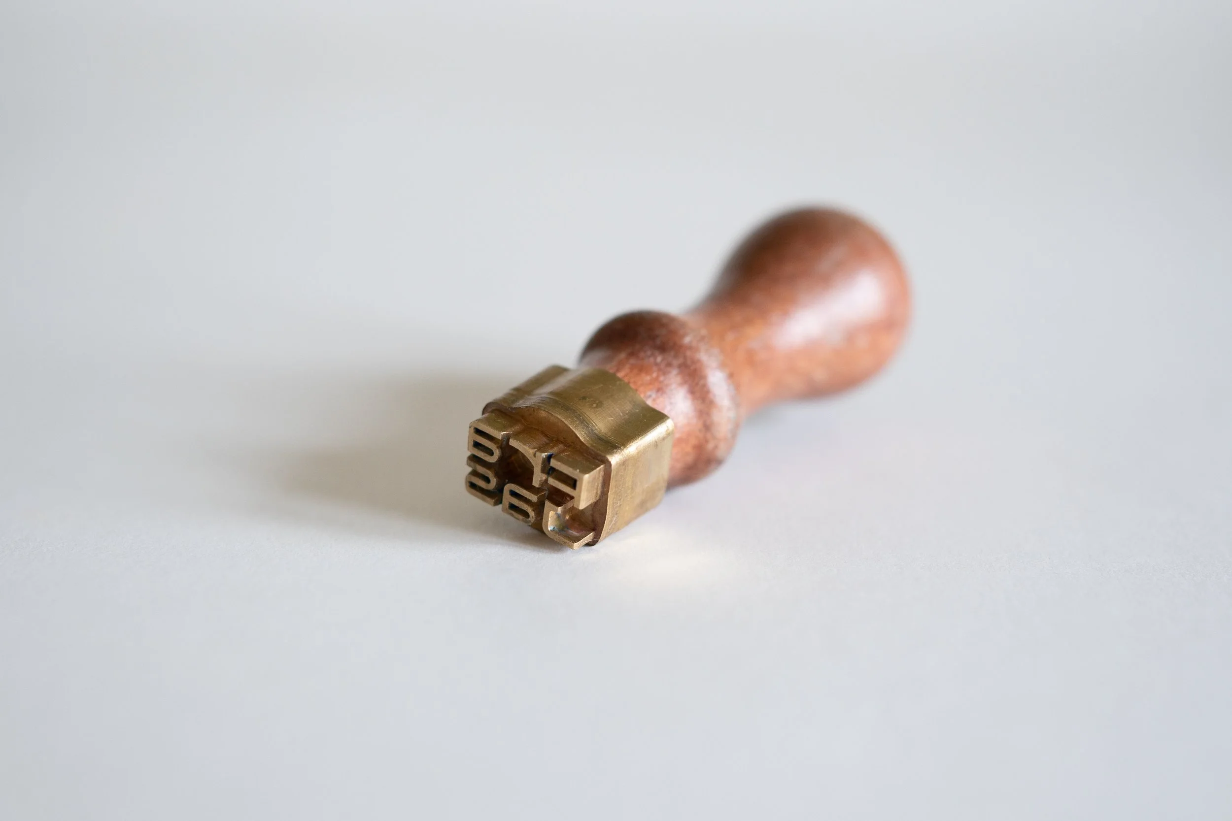 Close-up of a vintage metal stamp with a wooden handle on a plain white background.
